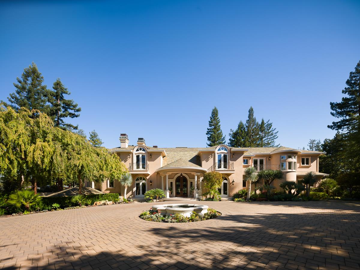 Large stucco home with arched entryways and a circular fountain in its paved courtyard.