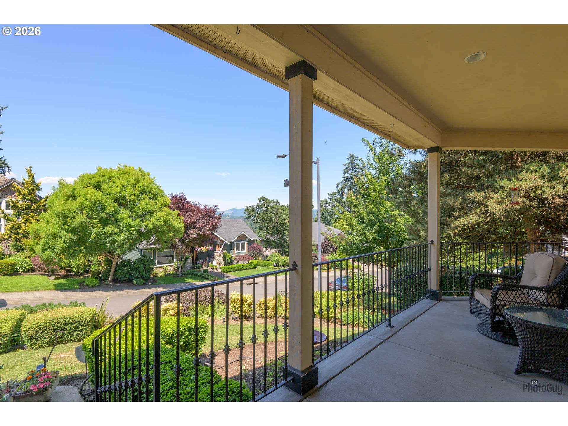Covered porch with wicker seating overlooks a leafy residential street and distant hills.