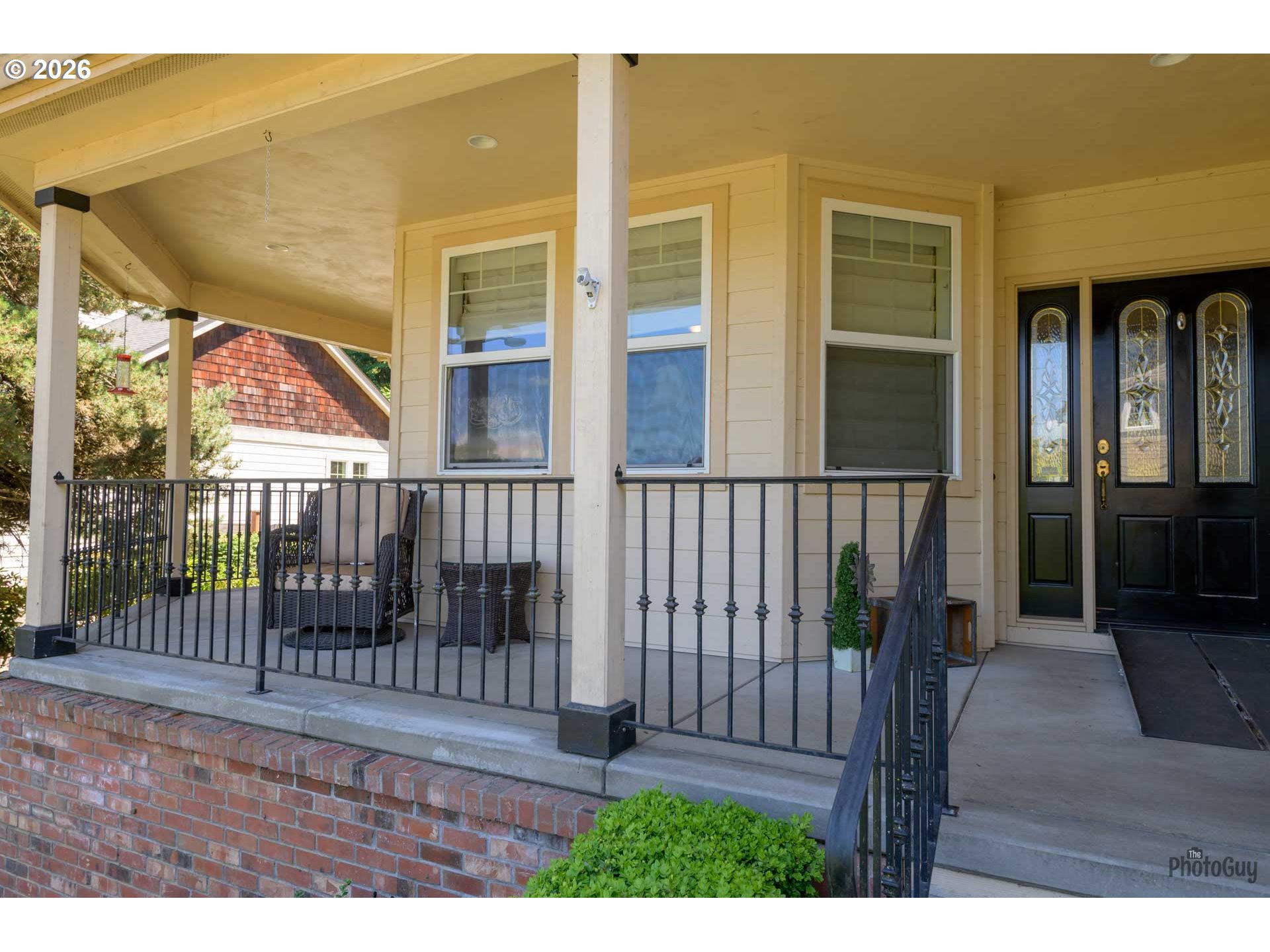 House front porch with black railings, brick steps, outdoor seating, and decorative glass entry doors.