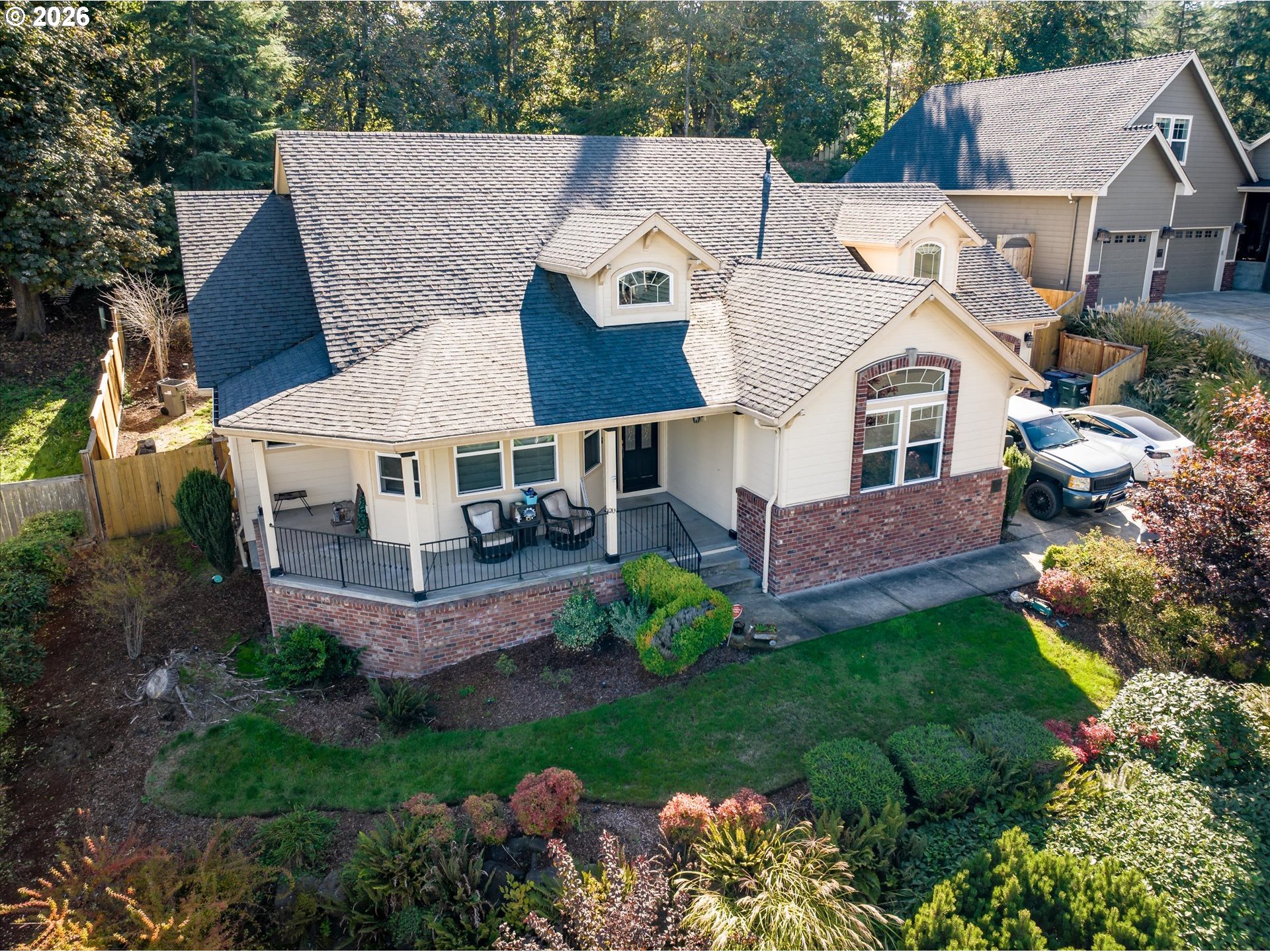 Aerial exterior of a cream house with a brick facade, covered porch, and landscaped lawn.