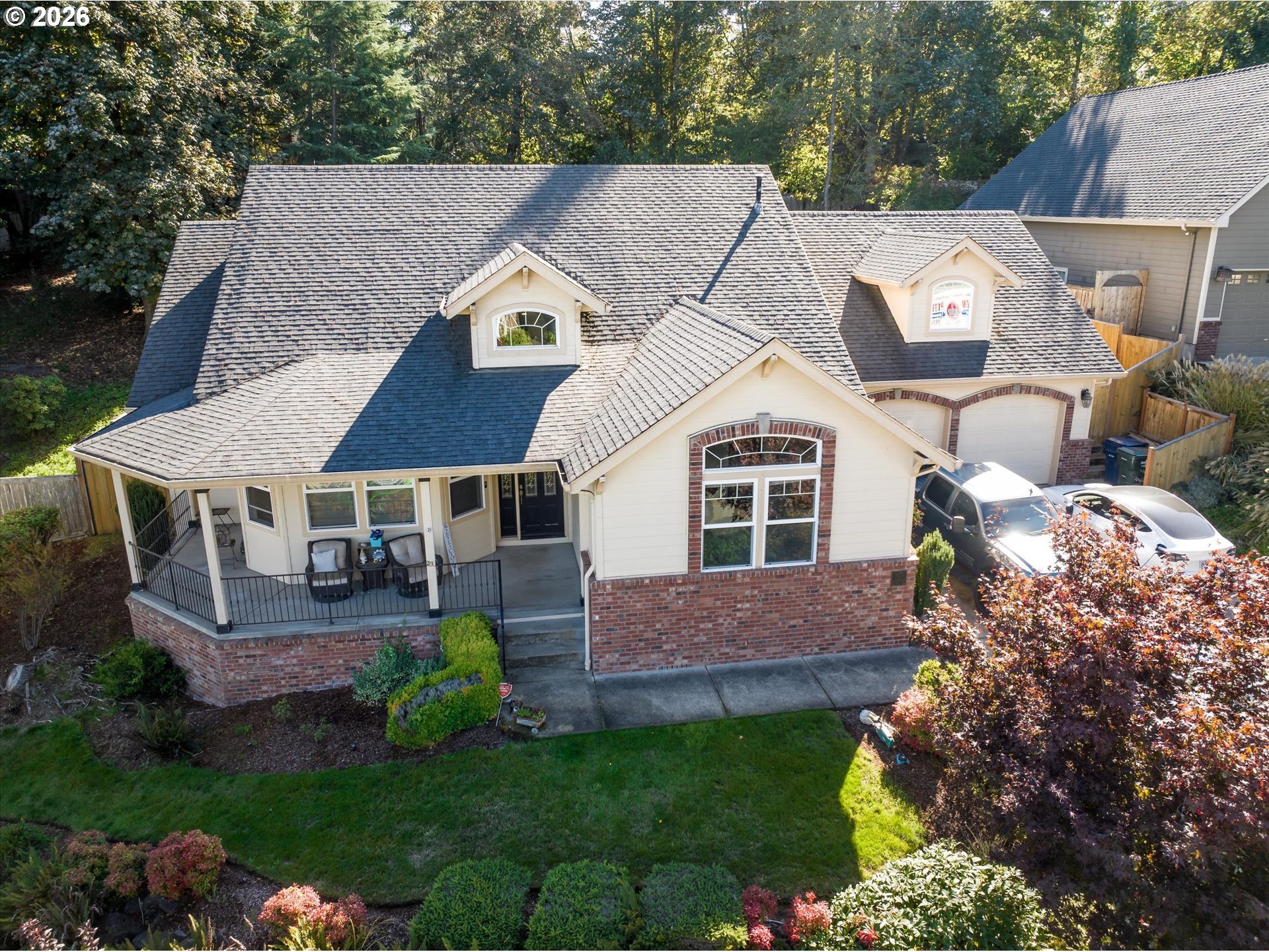 Aerial view of a cream-and-brick house with multiple gables, a covered porch, and landscaped lawn.