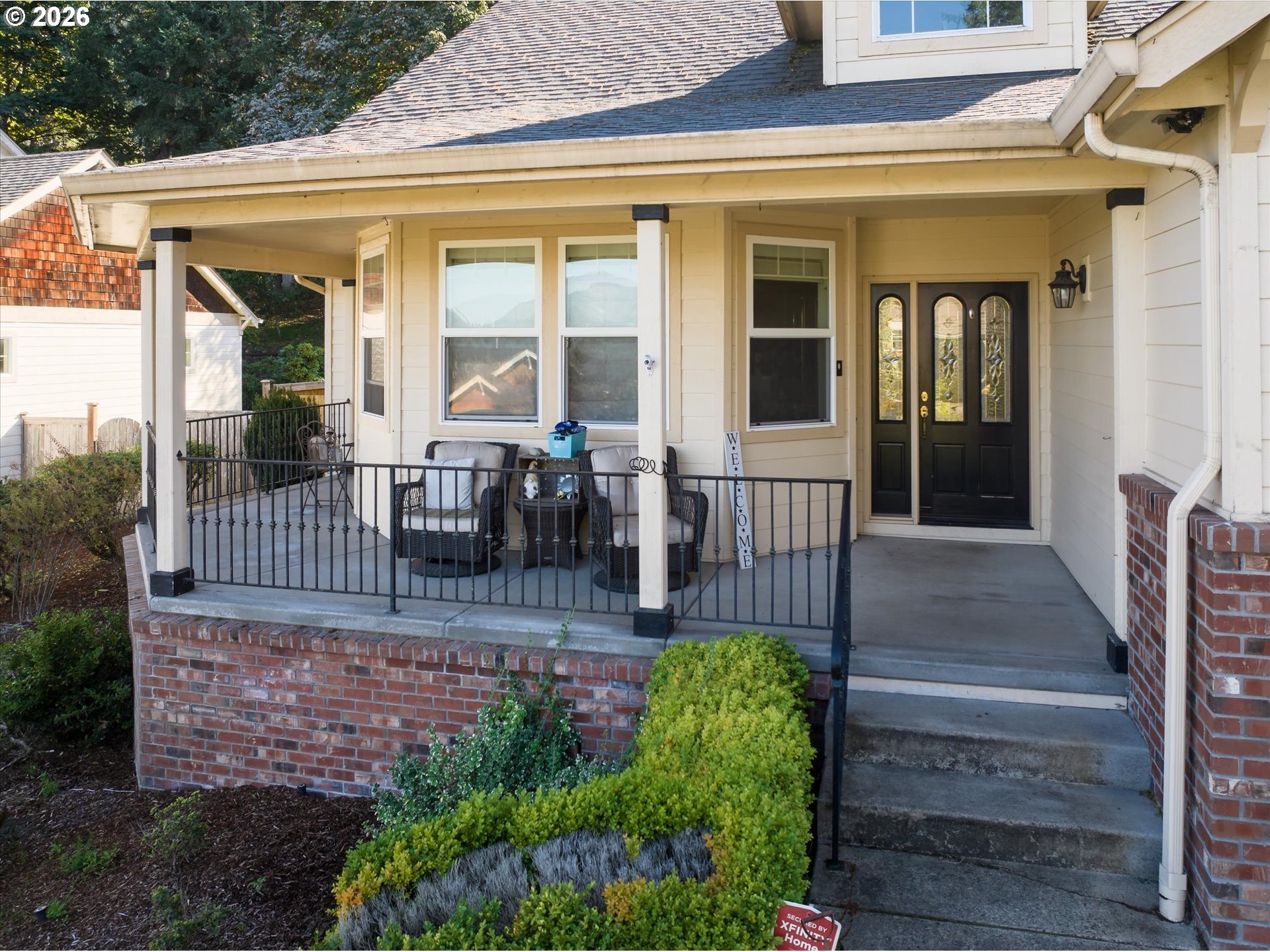 House with a covered porch, black railing and entry door, brick base, and landscaped steps.