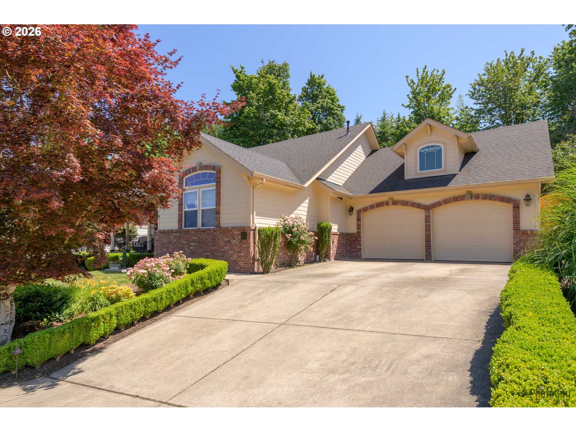 Beige two-story home with brick accents, double garage, and landscaped front garden.