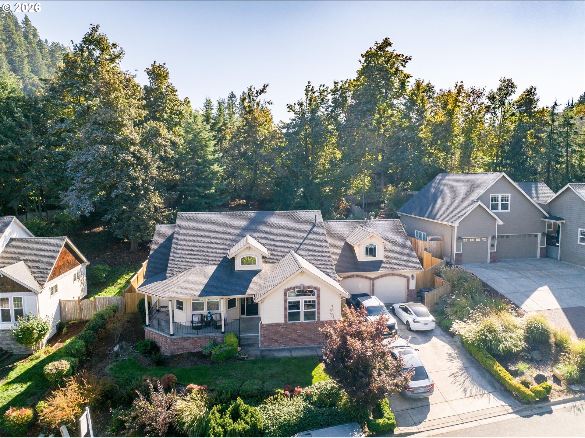Aerial view of a beige two-story home with brick accents, a covered porch, and landscaped yard.