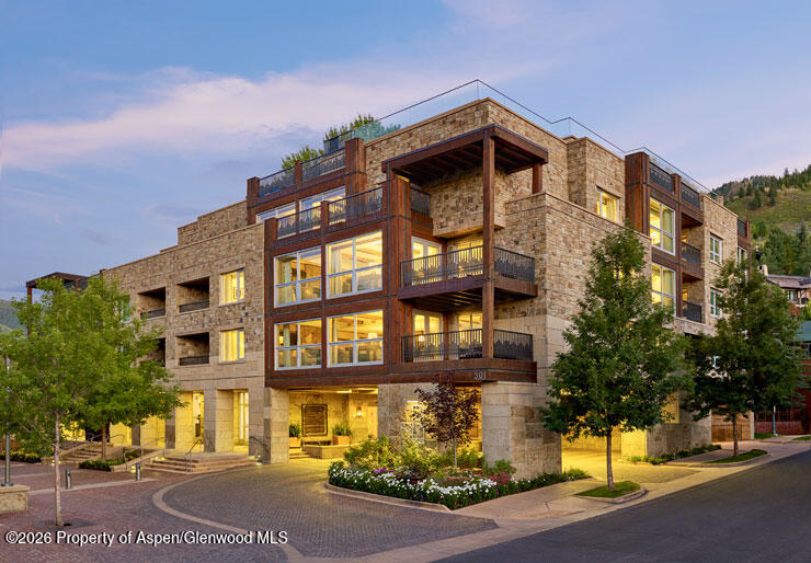 Modern stone-and-timber condominium building with projecting balconies and illuminated windows at dusk.