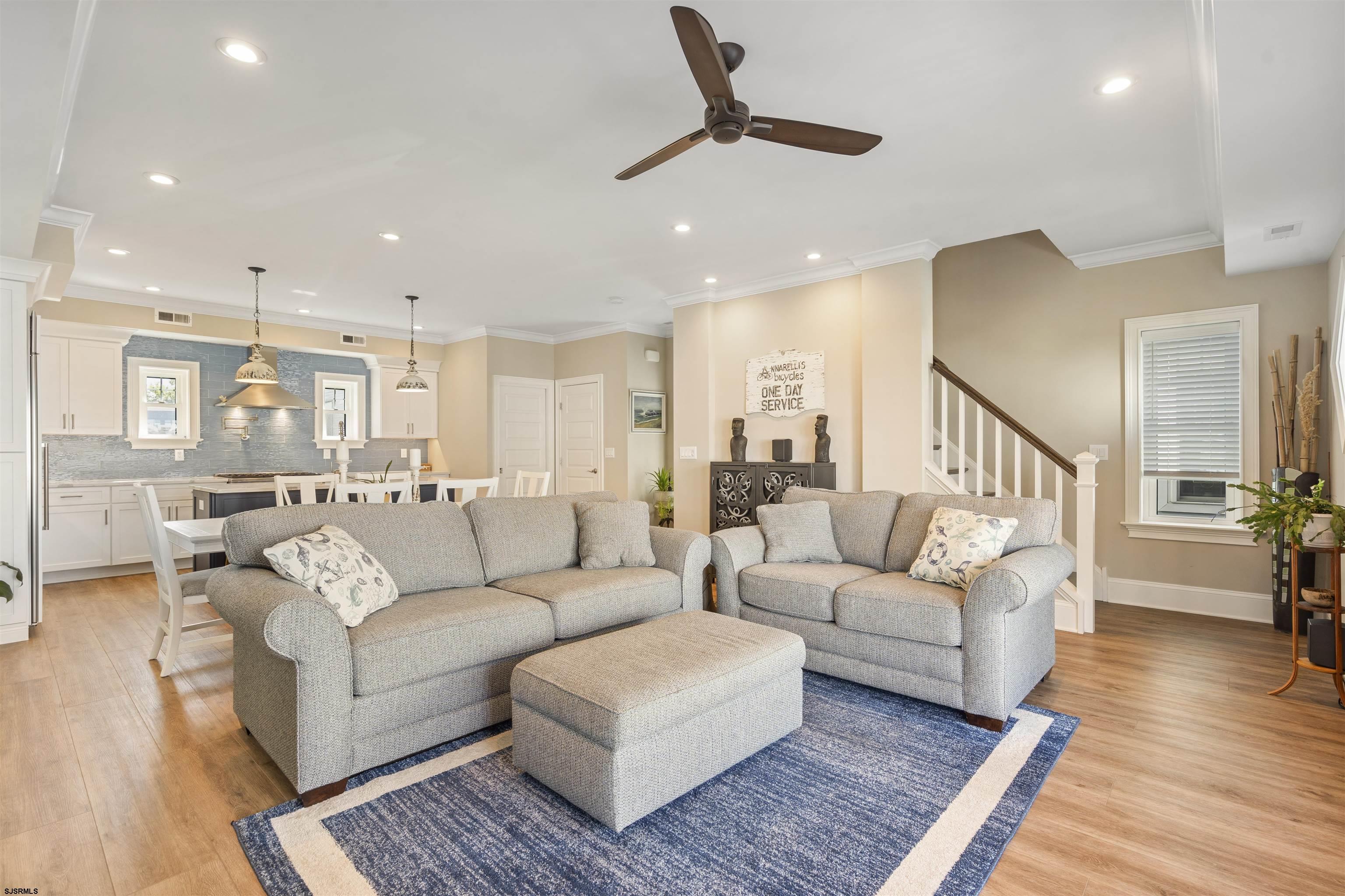 Open living room with gray sectional sofas and a blue rug beside a kitchen with a blue-gray tile backsplash.