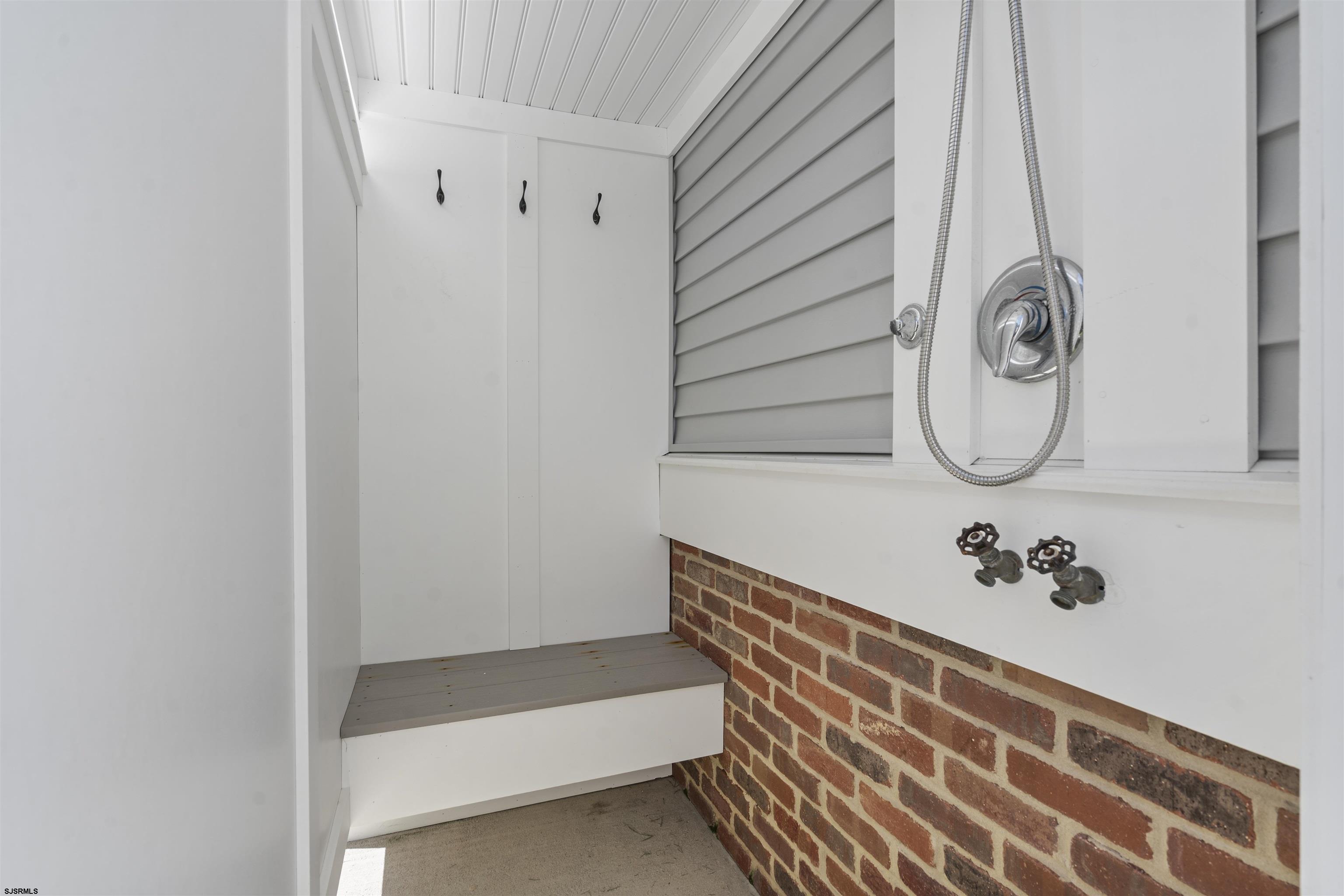 Outdoor shower with brick wall, handheld showerhead, and built-in bench.