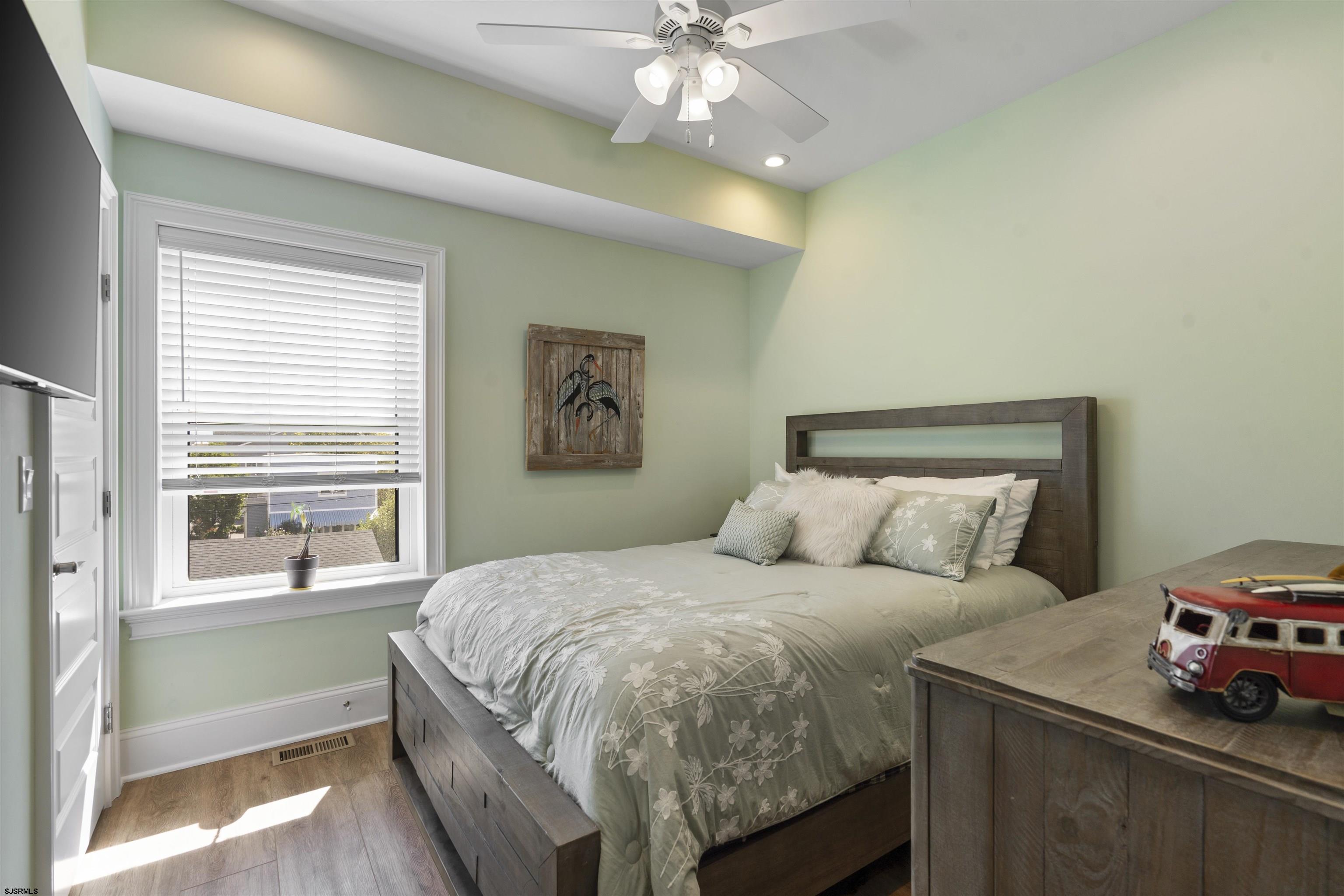 Bedroom with pale green walls, floral bedding, and a red model van on the dresser.