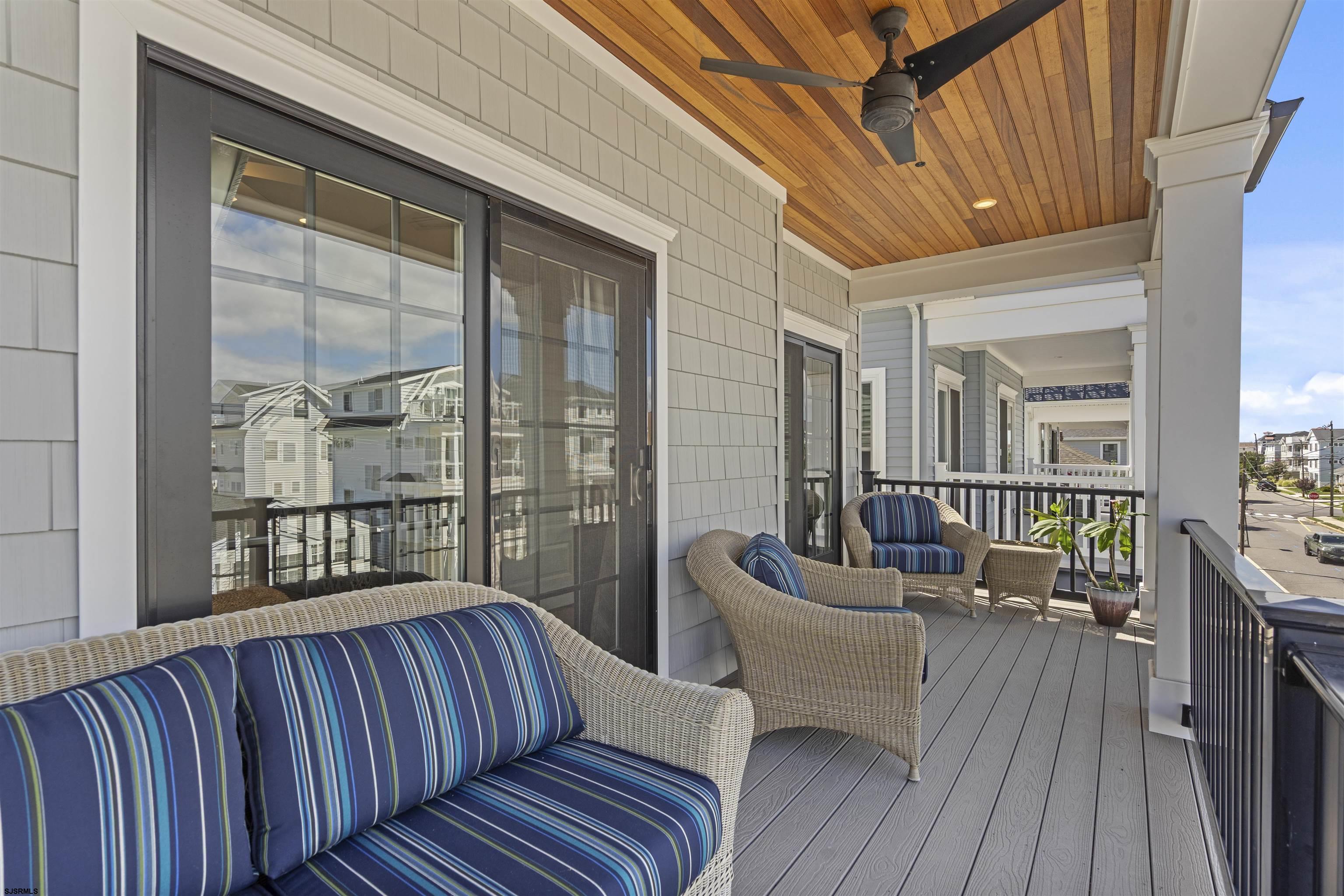 Covered porch with wicker seating, blue striped cushions, and a wood-plank ceiling.