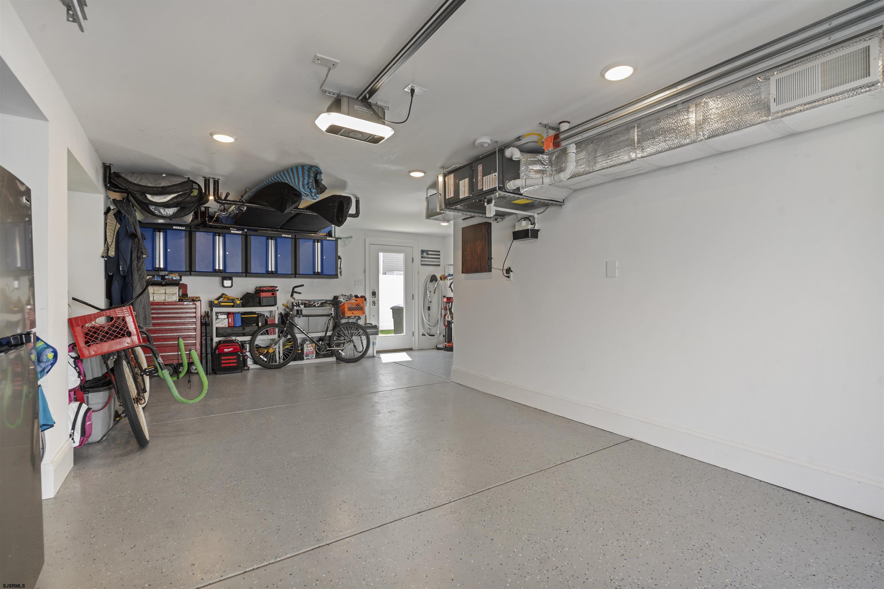 Garage with blue storage cabinets, bicycles, tools, and exposed ceiling ductwork.