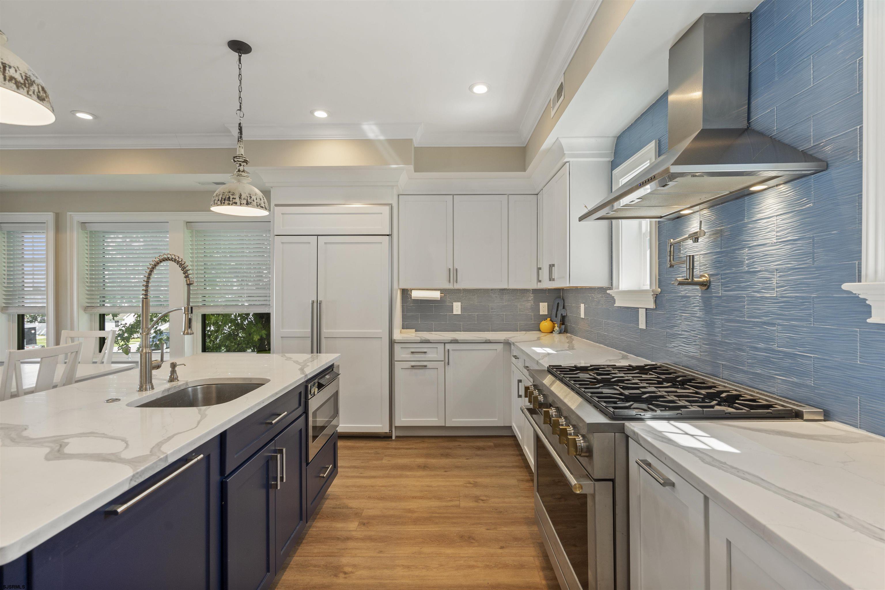 Kitchen with blue tile backsplash, navy island, white cabinets, and a large stainless steel range.