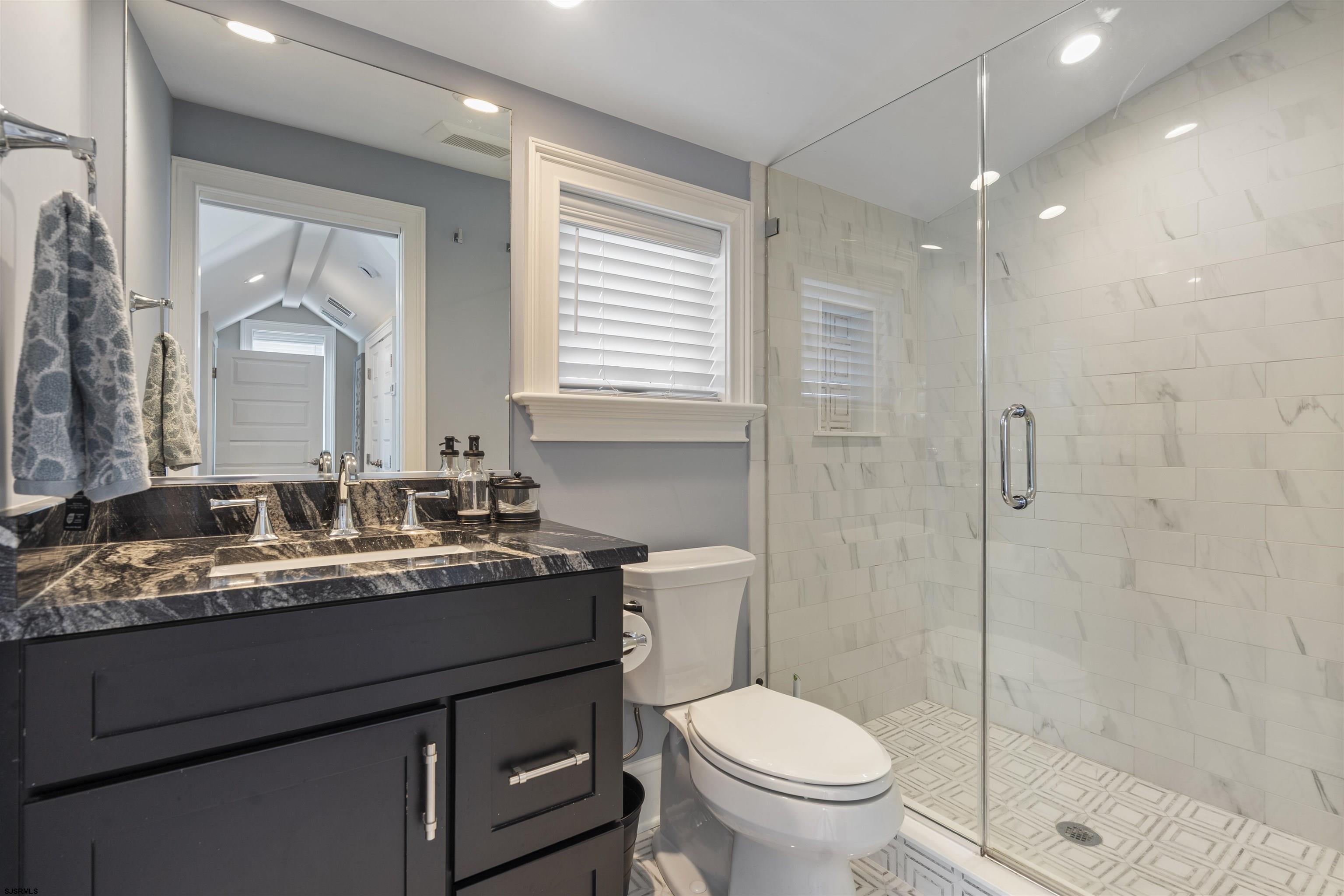 Bathroom with a dark vanity, black marble countertop, and glass-enclosed marble-look shower.