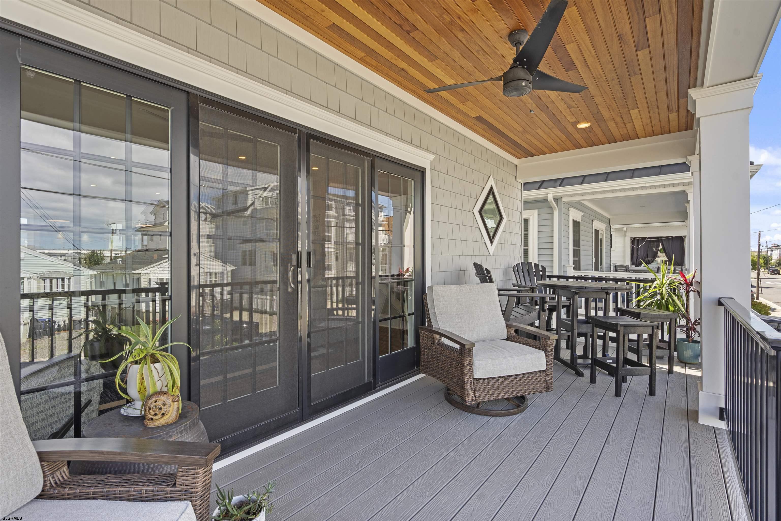 Covered porch with gray decking, a wood ceiling and fan, wicker seating, and an outdoor dining set.