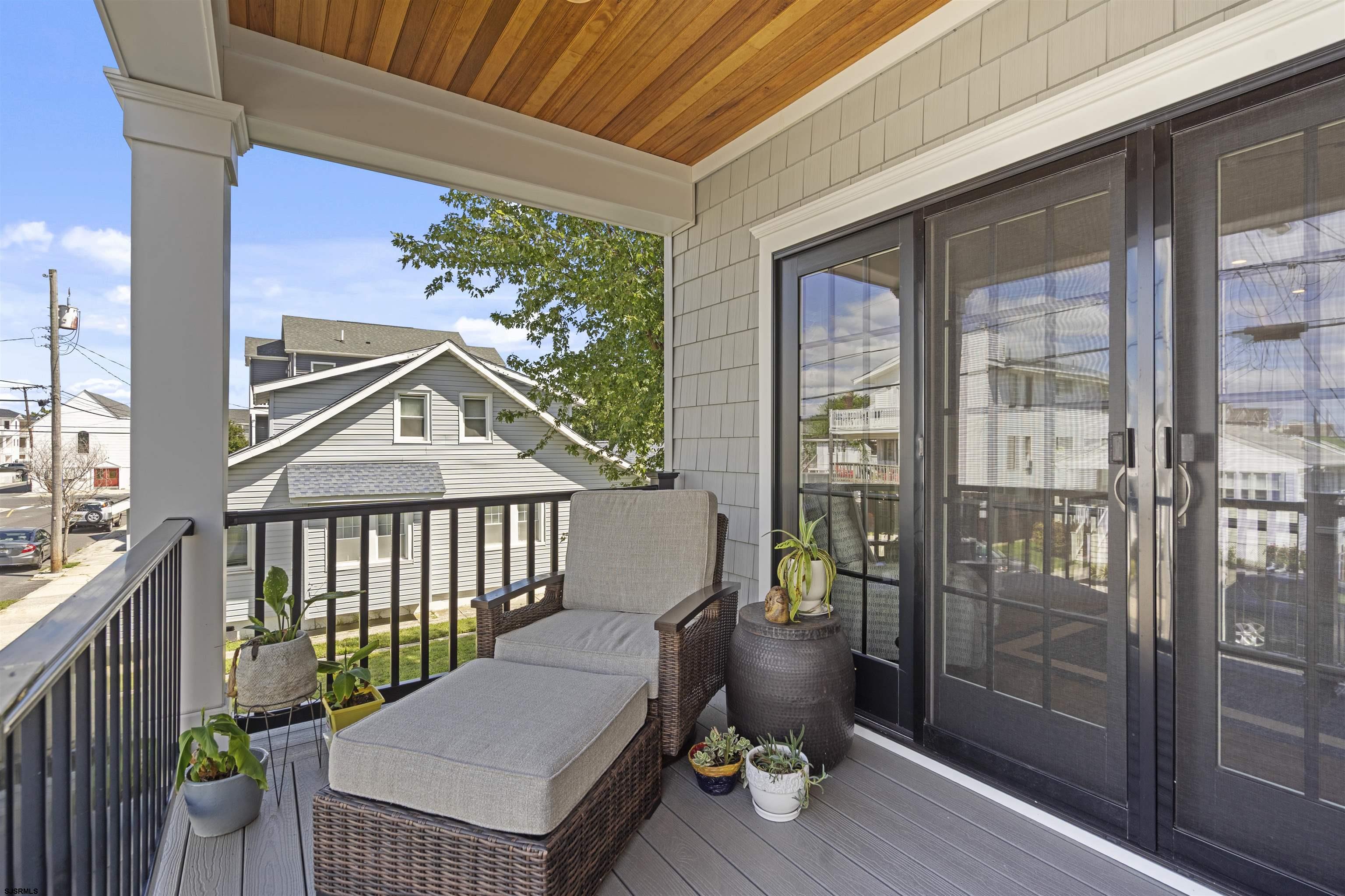 Covered porch with wicker lounge seating, potted plants, and dark sliding screen doors.