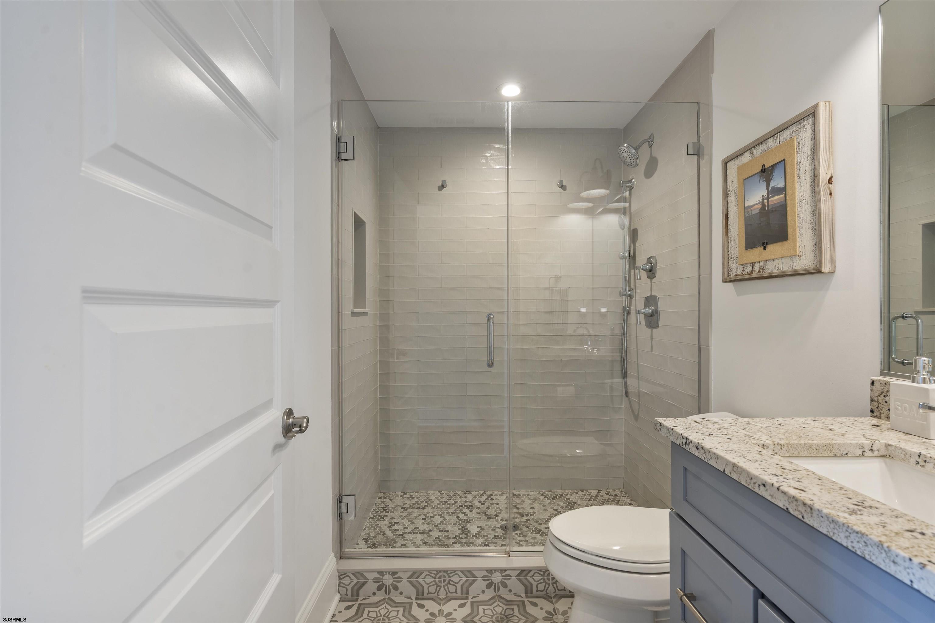 Bathroom with a glass-enclosed tiled shower, patterned floor, and blue vanity with stone countertop.