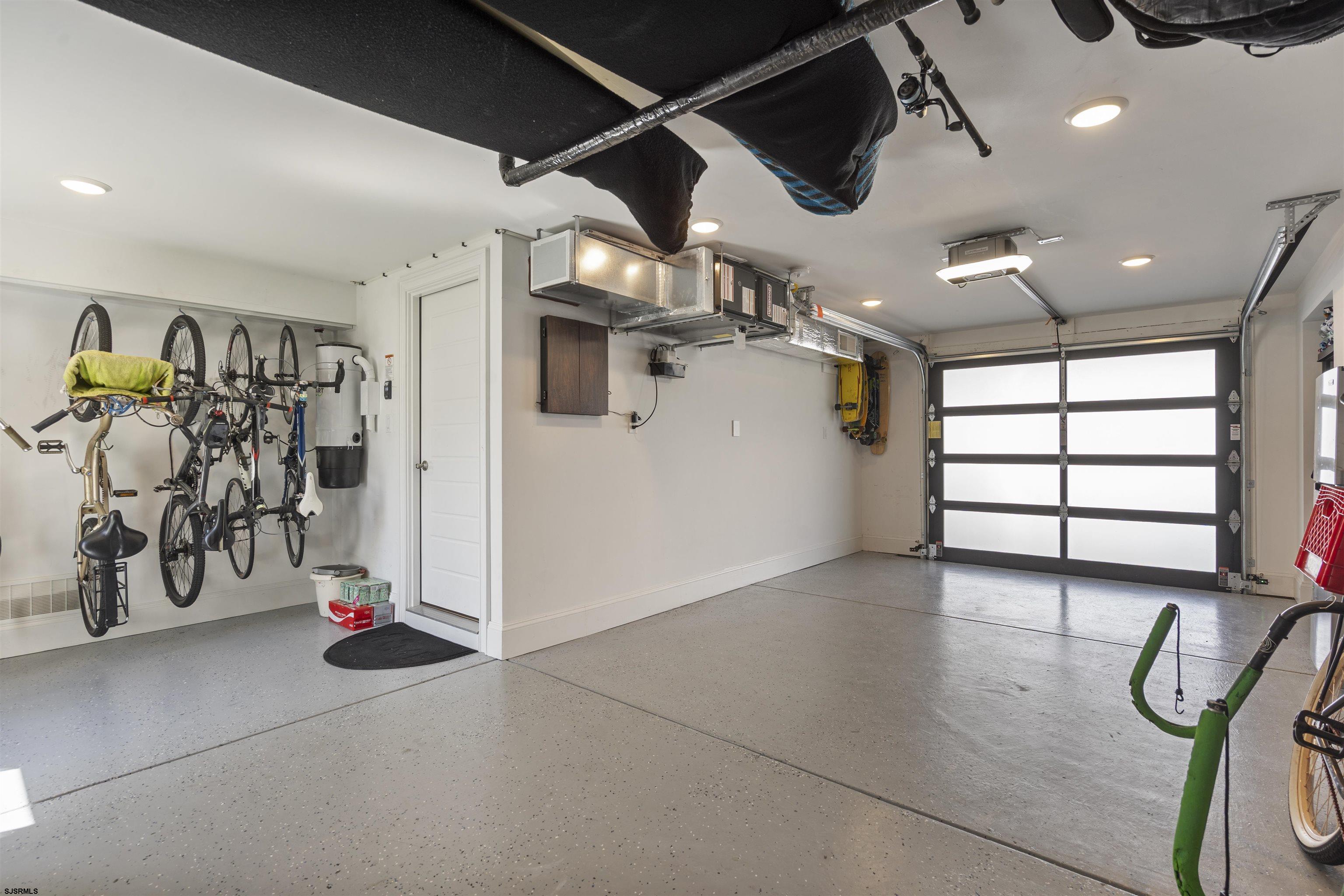 Spacious garage with hanging bicycles, overhead storage, and a black-framed garage door.