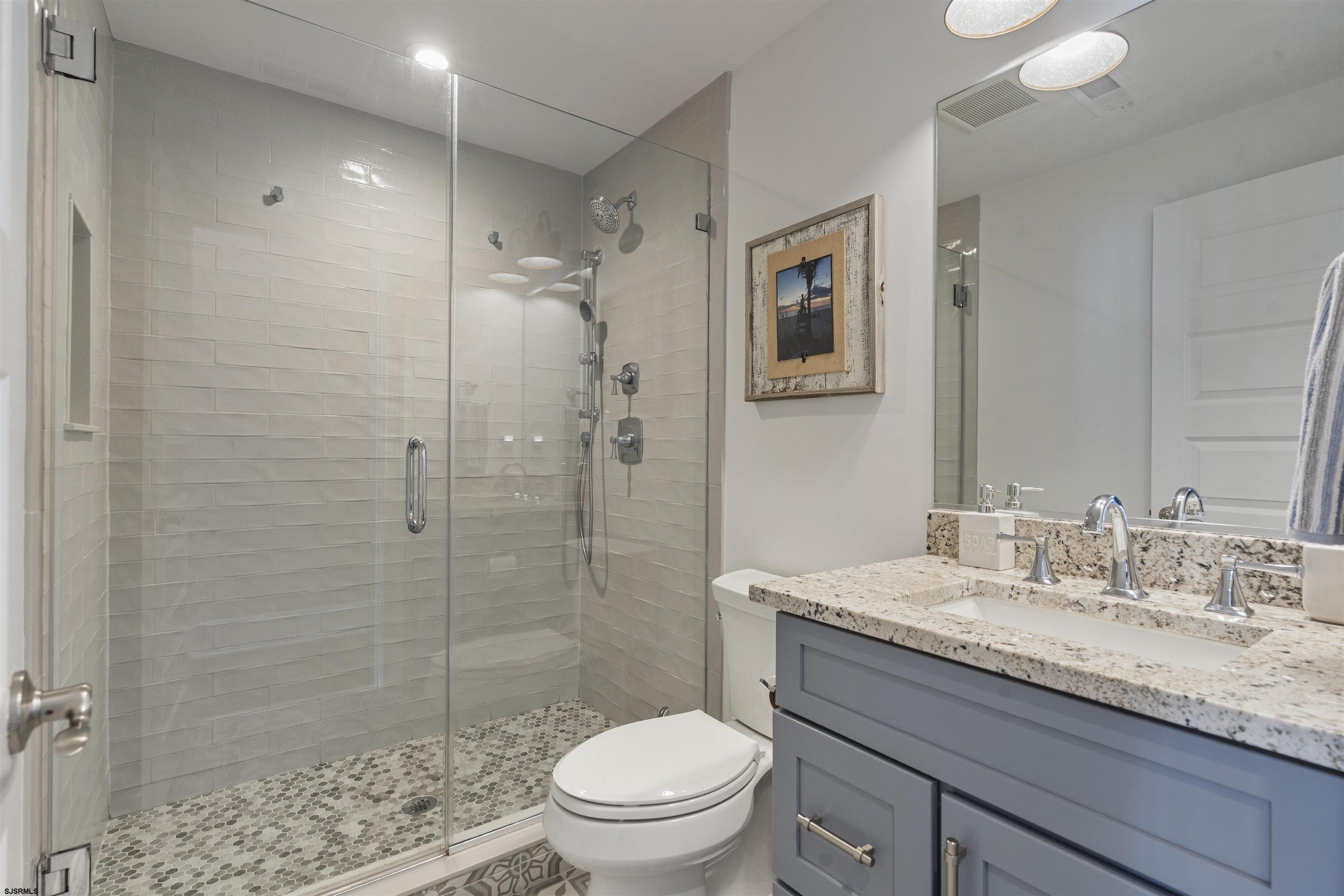 Bathroom with a glass-enclosed tiled shower and blue-gray vanity topped with granite.