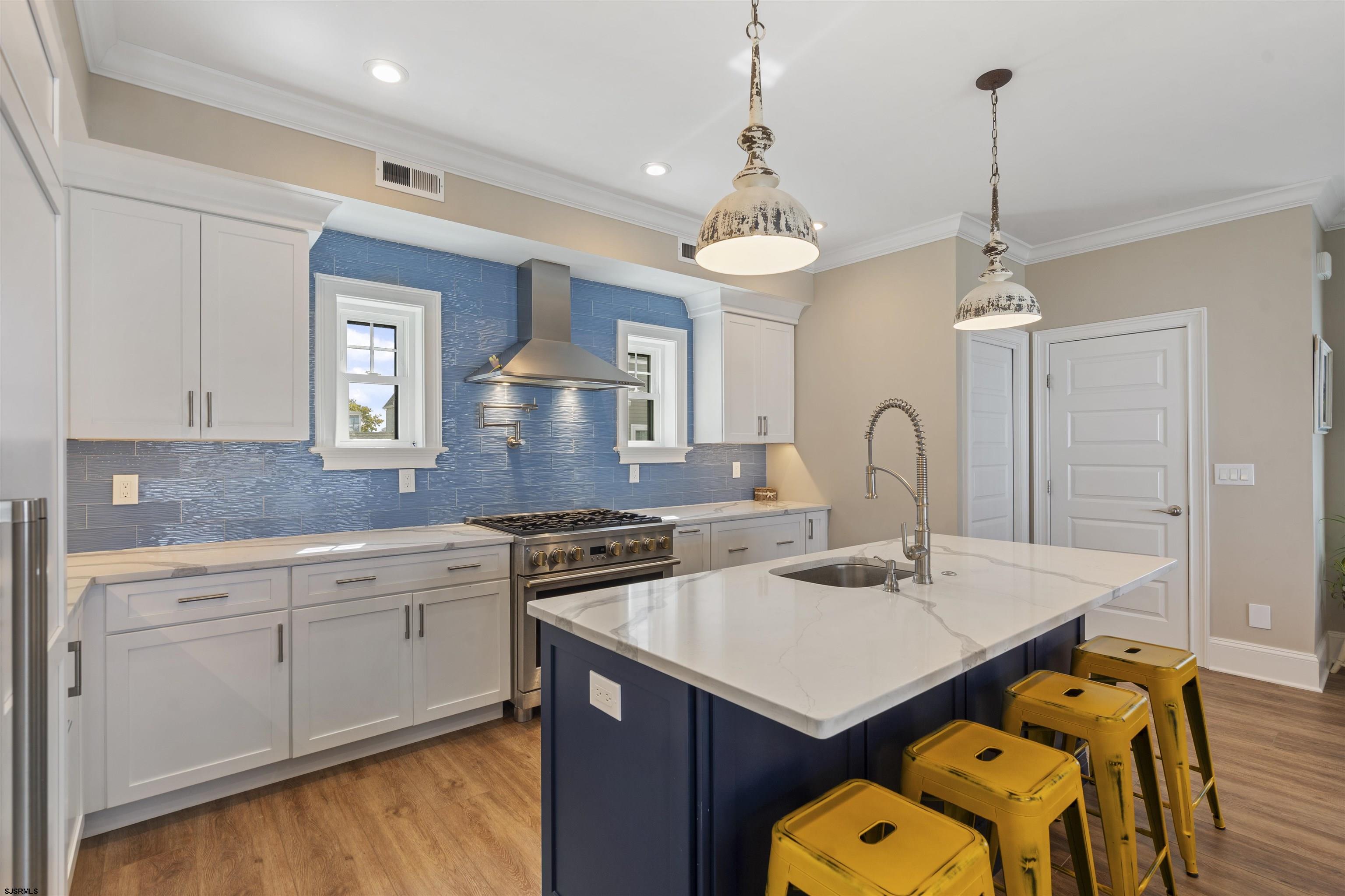 Kitchen with a blue tile backsplash, large navy island, white cabinets, and yellow stools.