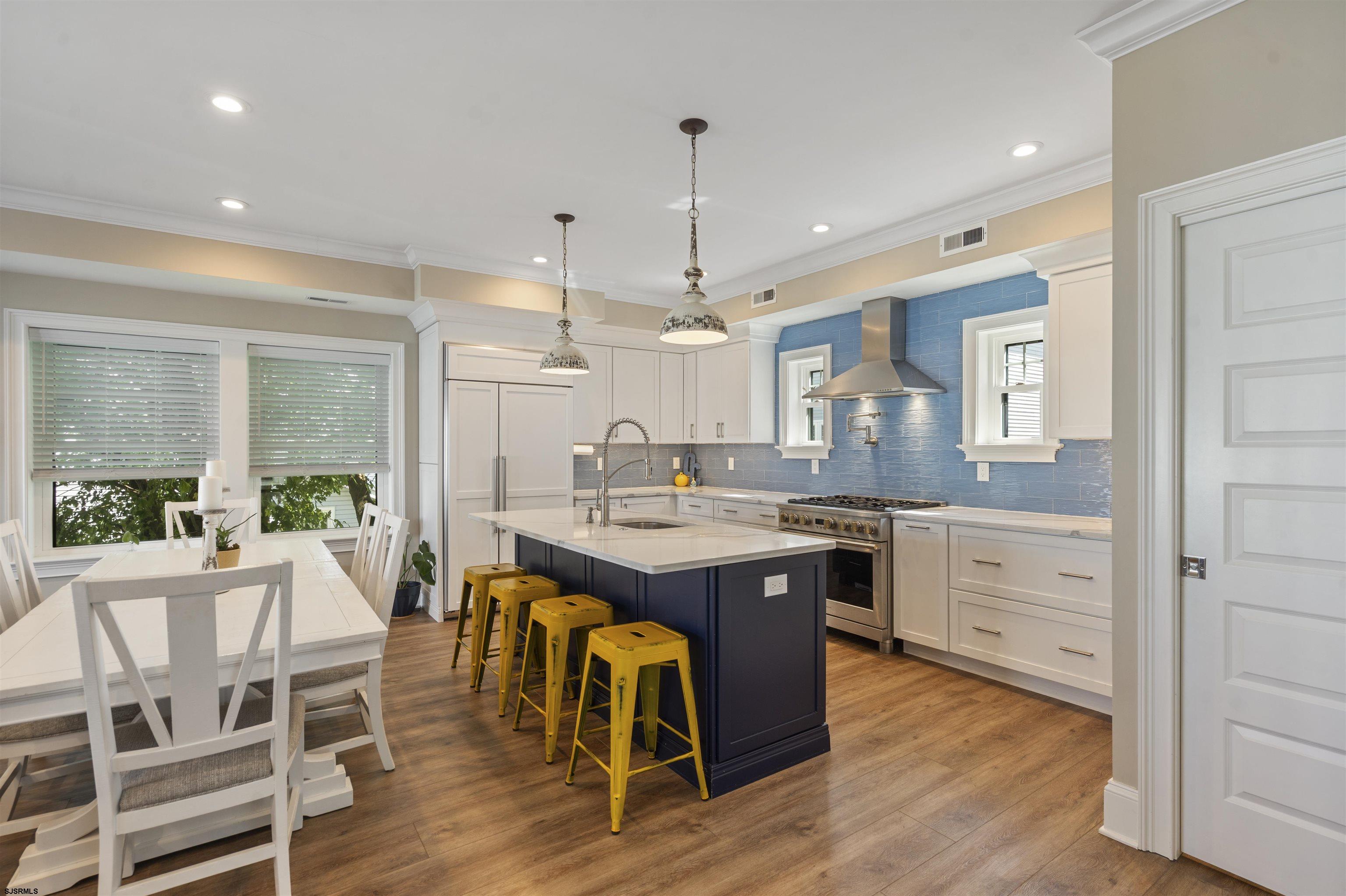 Kitchen with blue tile backsplash, white cabinetry, and a dark island lined with yellow stools.
