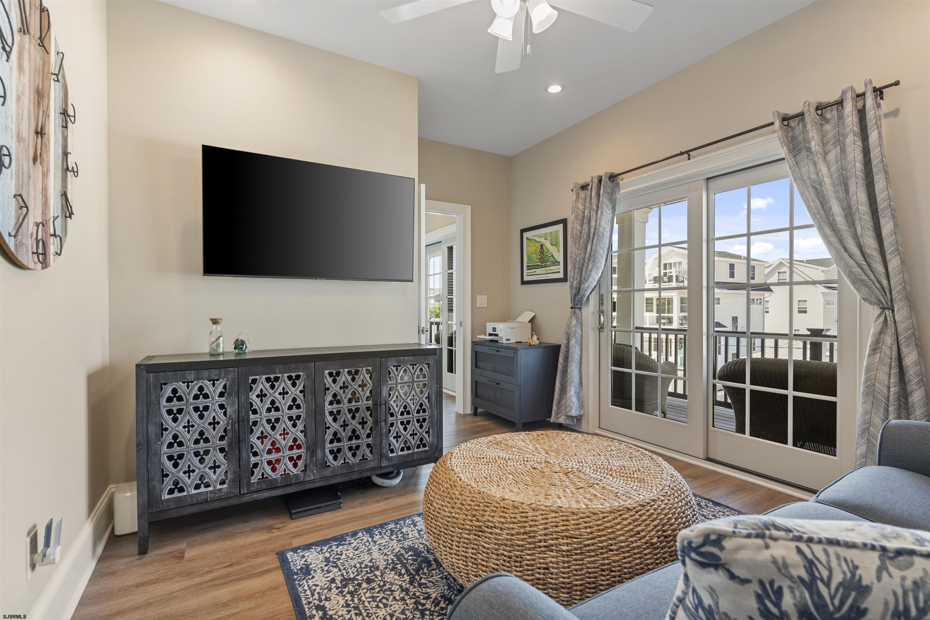 Living room with a wall-mounted television, woven ottoman, and French doors opening to a balcony.
