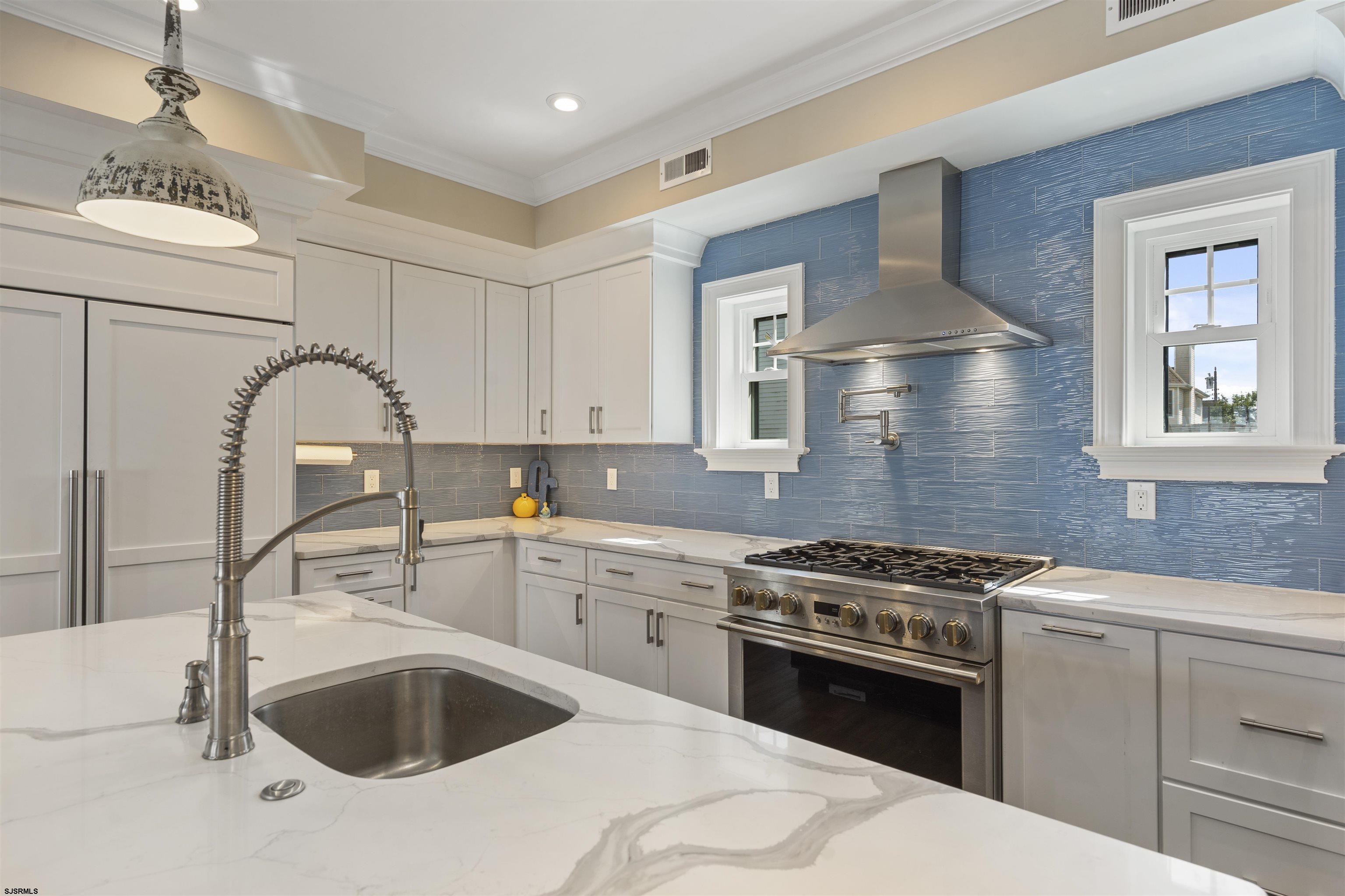 Kitchen with blue tile backsplash, white cabinetry, quartz island, and stainless steel range.