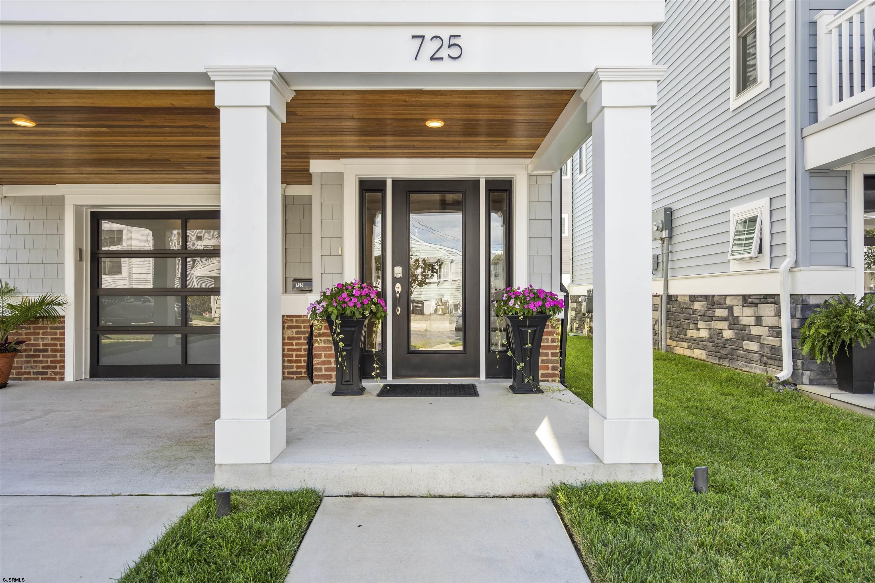 Covered front entrance with dark glass-paneled door, white columns, wood ceiling, and flower planters.