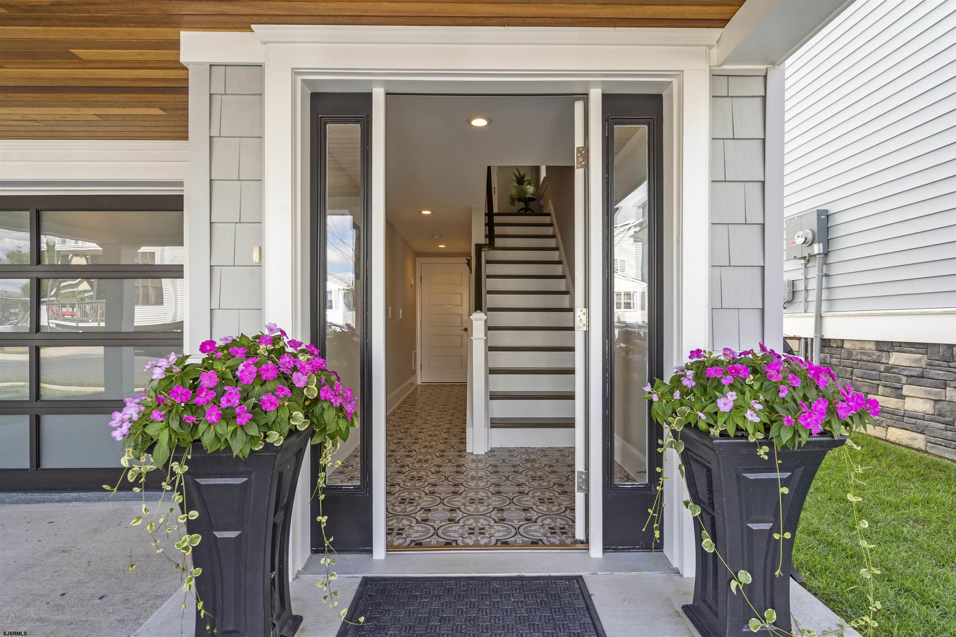 Home entrance with pink flower planters, patterned tile flooring, and a staircase beyond the open door.