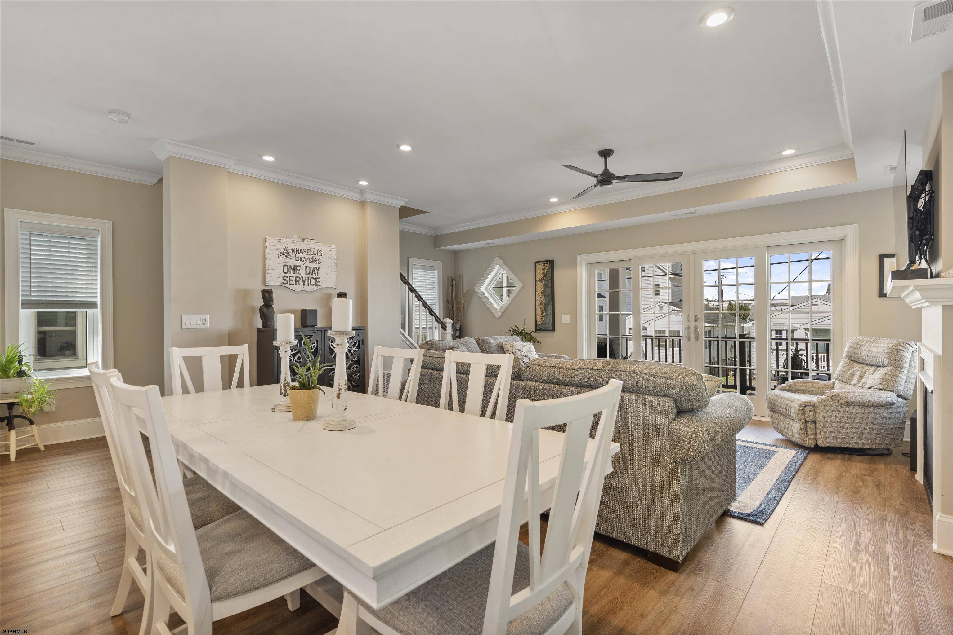 Open-plan living and dining room with a white table, gray sectional, and glass doors to a balcony.