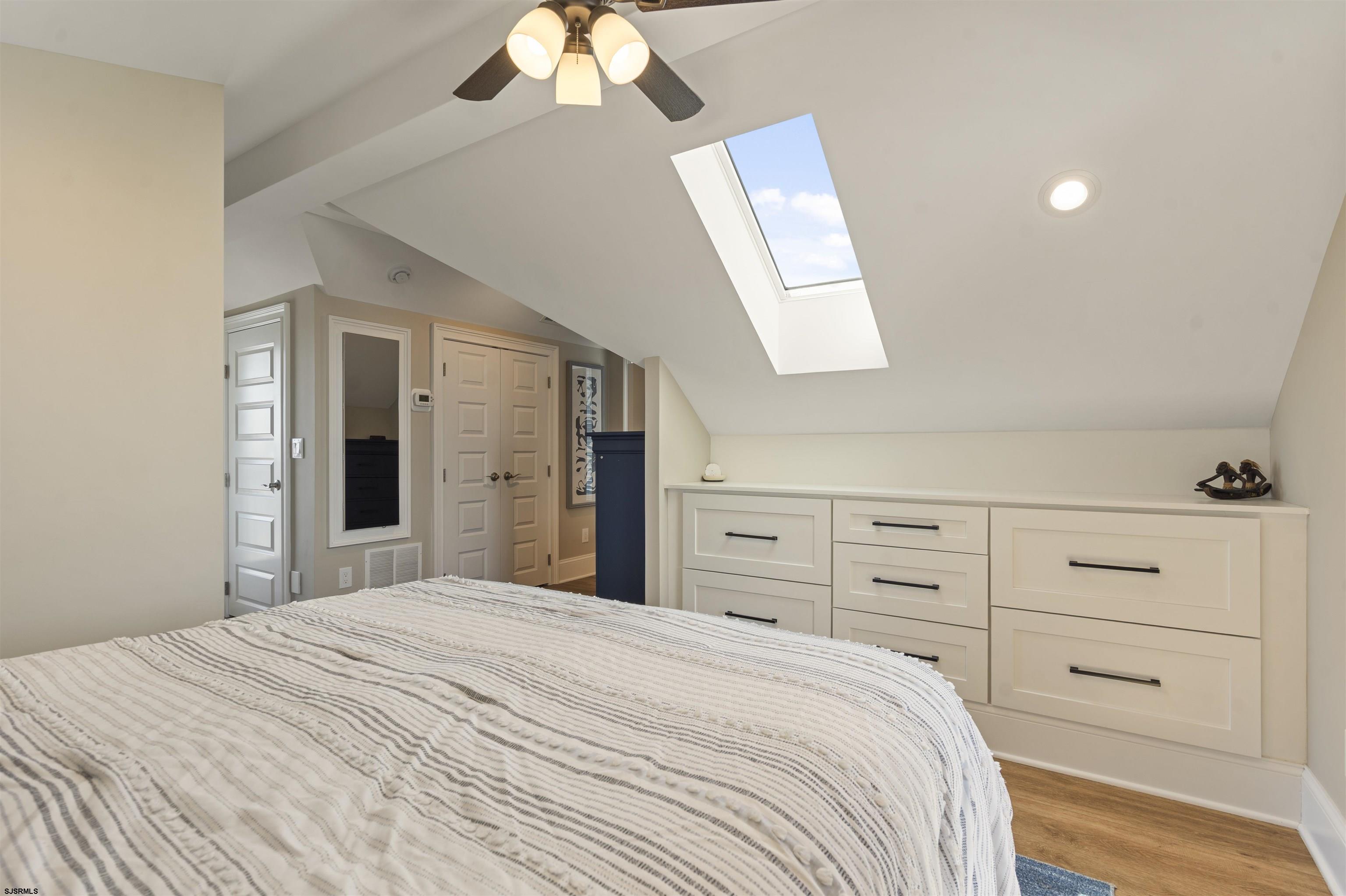 Bedroom with built-in drawers and a skylight above a striped bed.