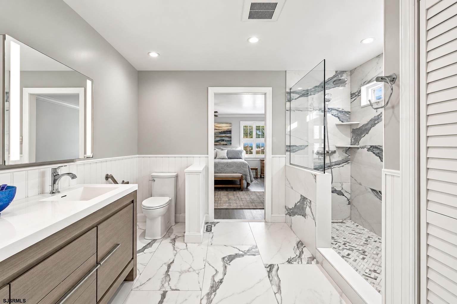 Renovated bathroom with a glass shower, veined marble-look tile, and a wood-tone vanity.