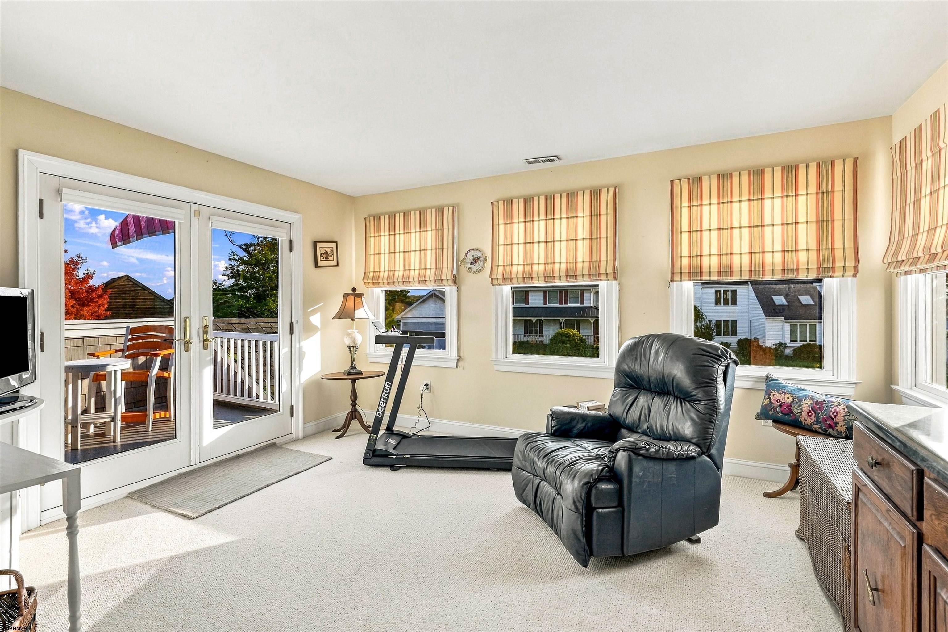 Bright sitting room with French doors to a deck, striped shades, a leather recliner, and a treadmill.
