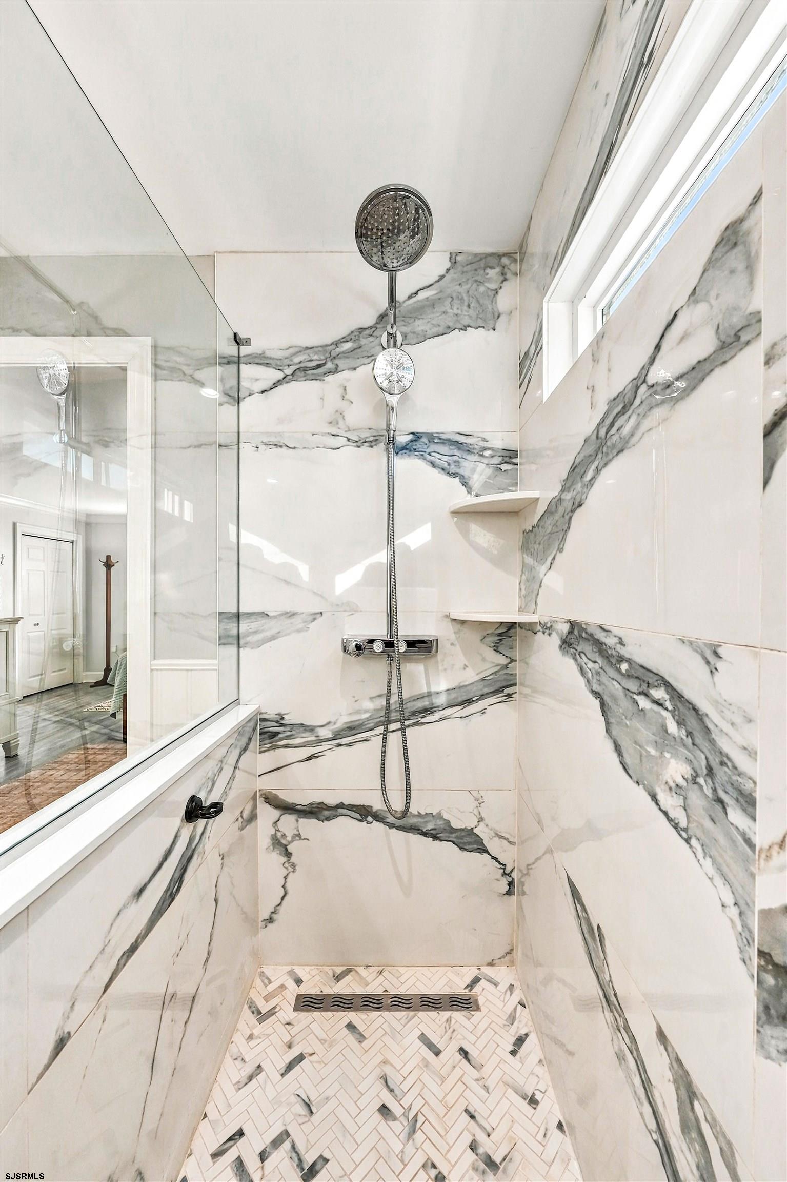 Marble-tiled walk-in shower with chrome showerheads and a herringbone mosaic floor.