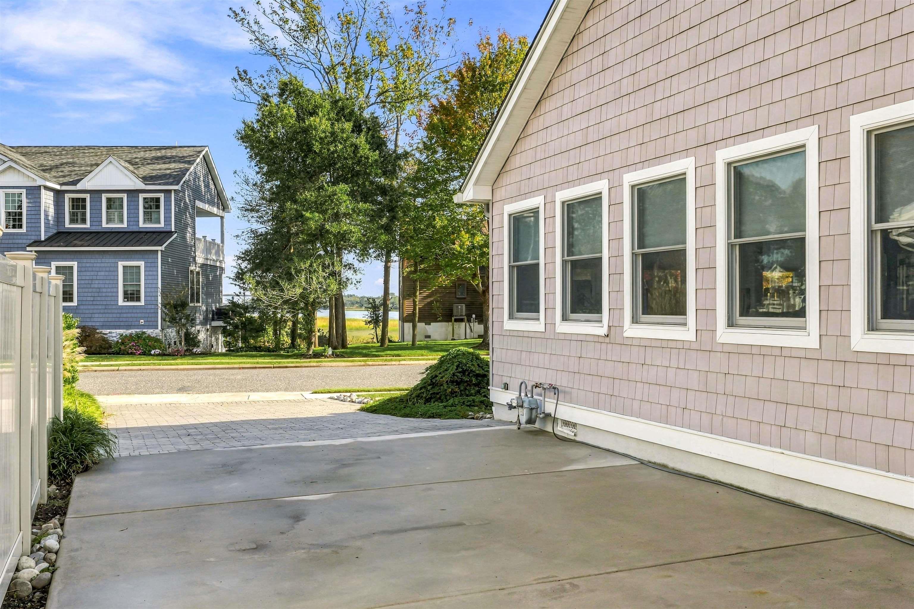 Shingle-sided home beside a concrete driveway, with neighboring houses and a glimpse of water across the street.