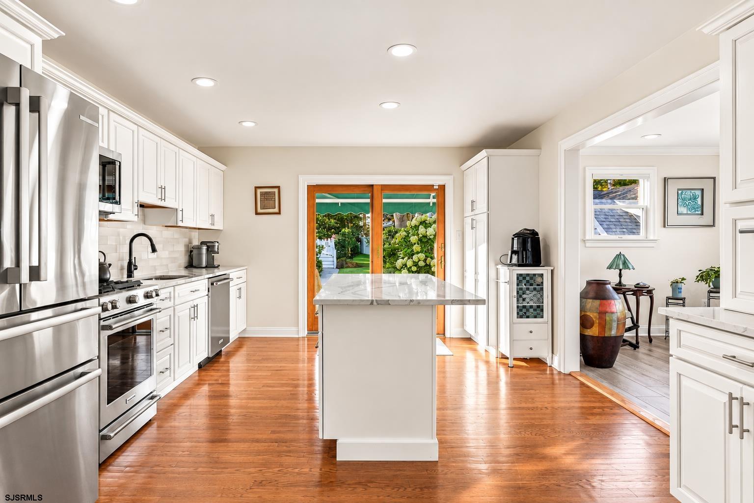Kitchen with white cabinets, stainless steel appliances, marble island, and garden-facing sliding doors.