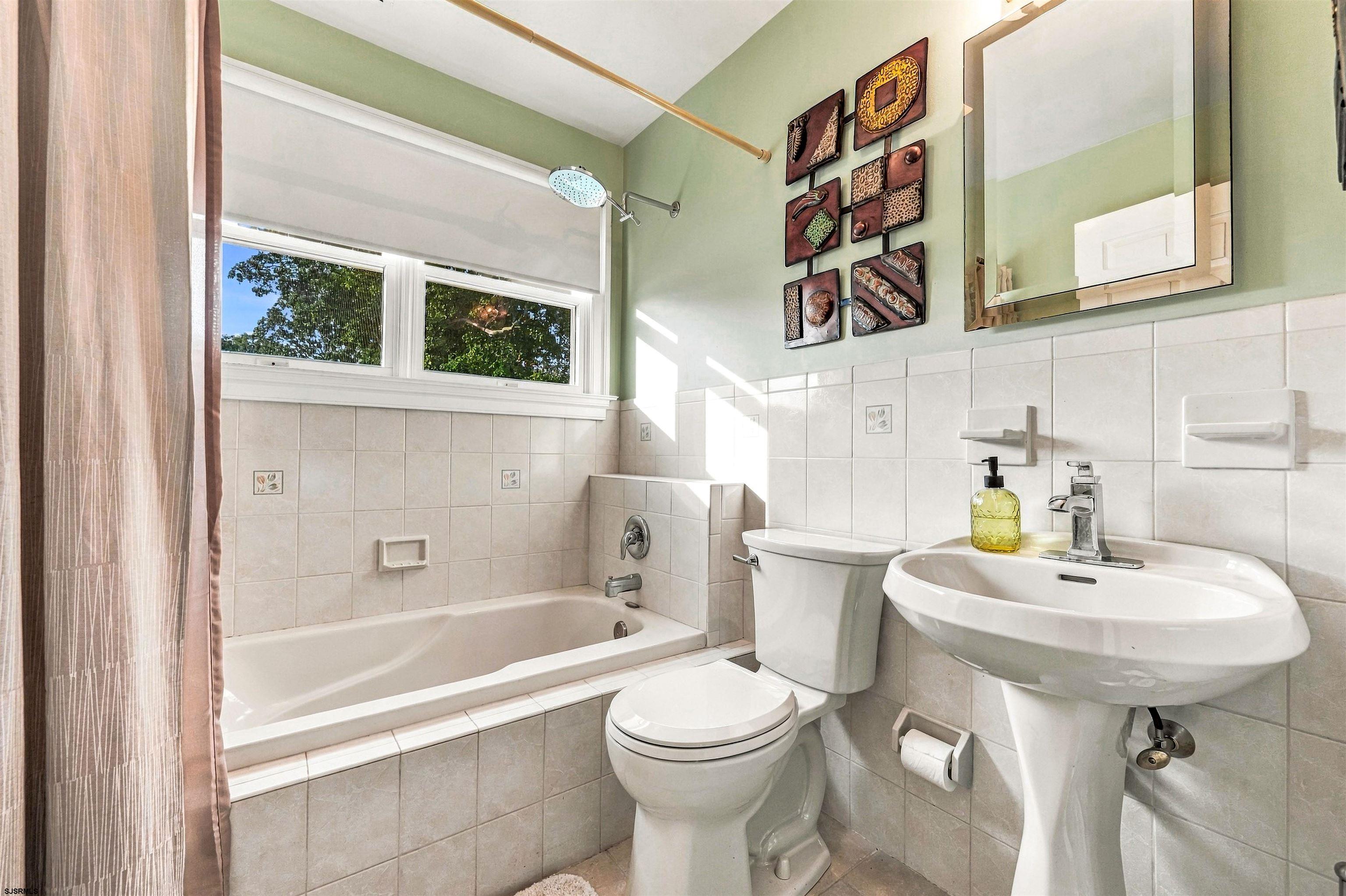 Bathroom with a tiled bathtub, pedestal sink, and wide sunny window.