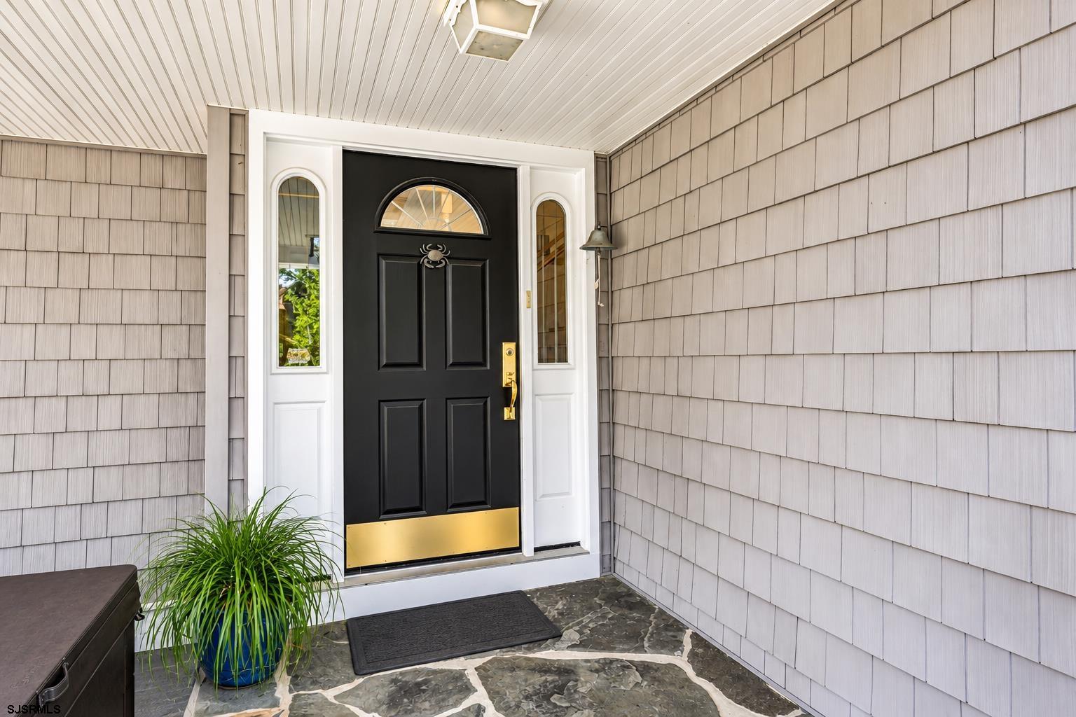 Covered entry with a black front door, brass accents, narrow sidelights, and a potted plant.
