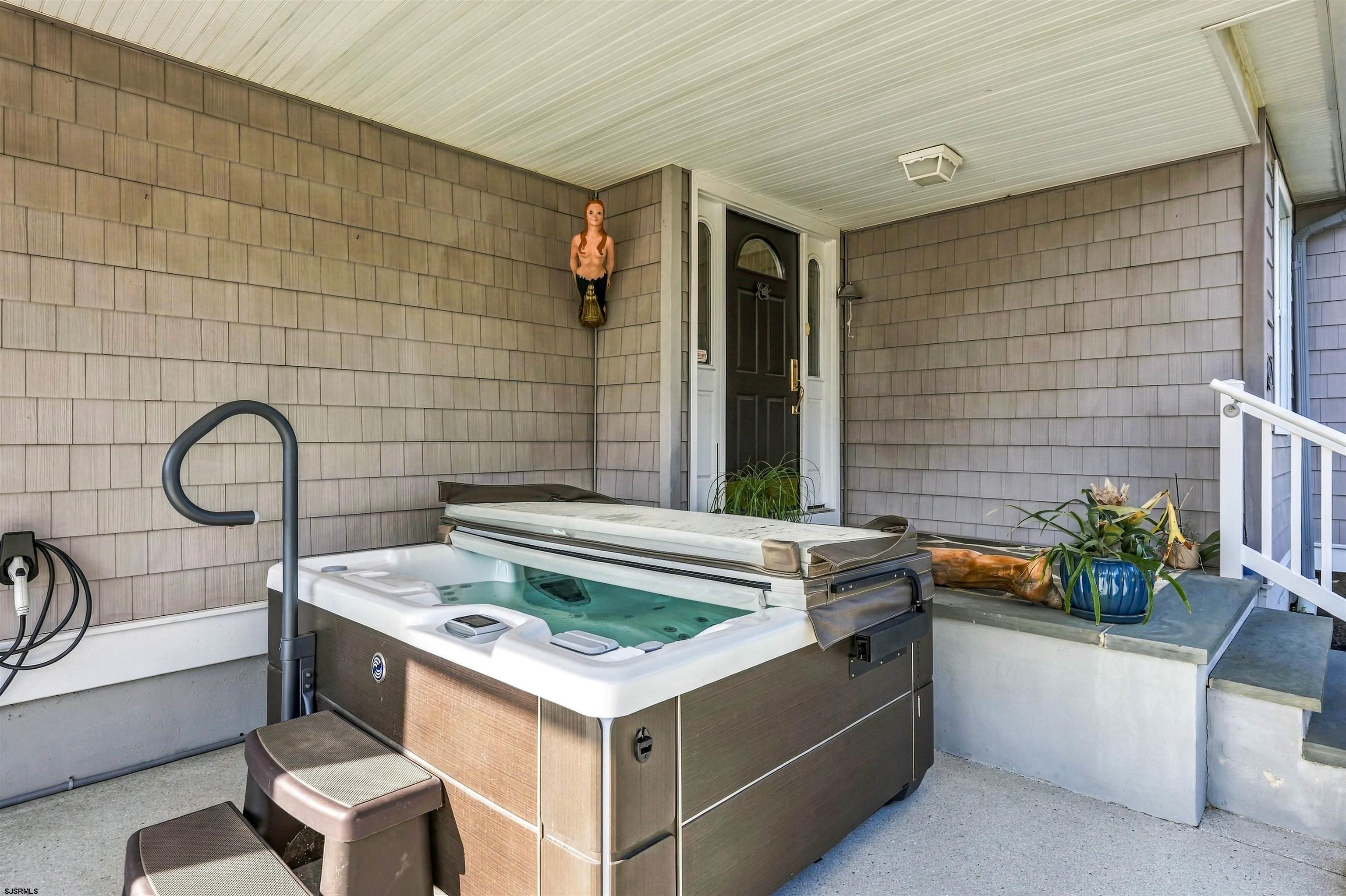 Covered porch with a large hot tub, entry door, and potted plants.