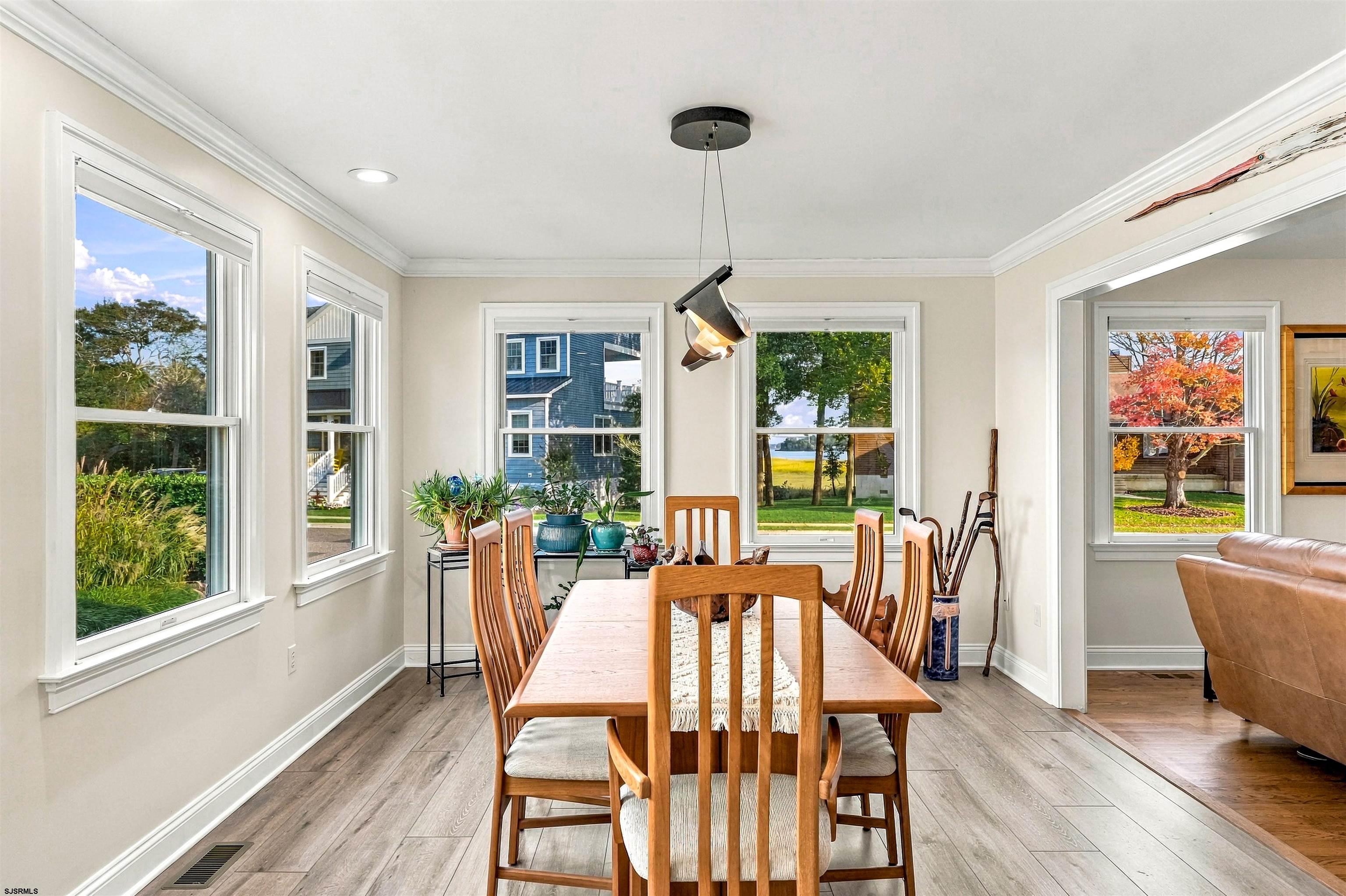 Dining room with a wooden table and chairs, large windows, and a glimpse of water outside.