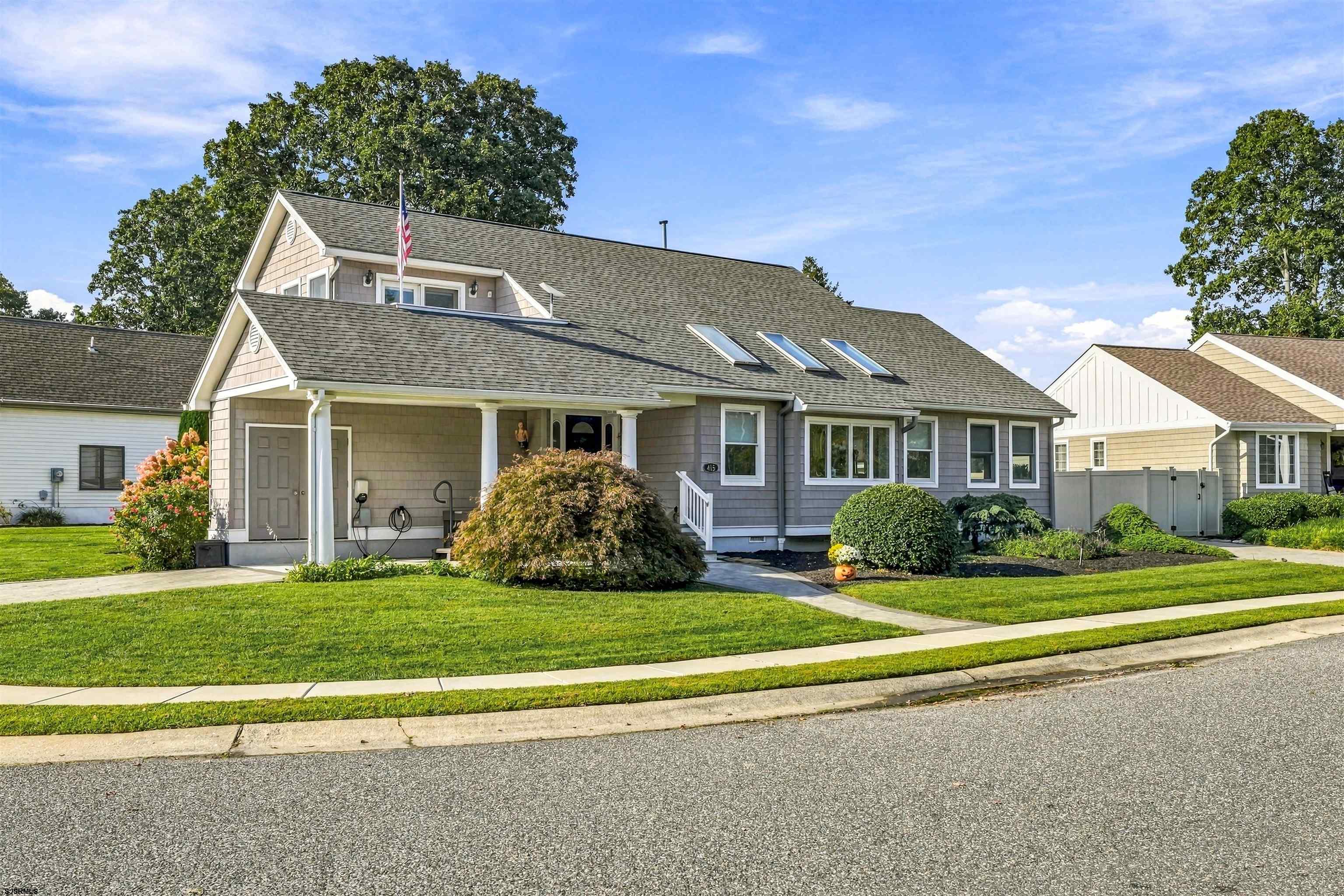 Gray shingle-sided home with a covered entry, roof skylights, landscaped lawn, and American flag.