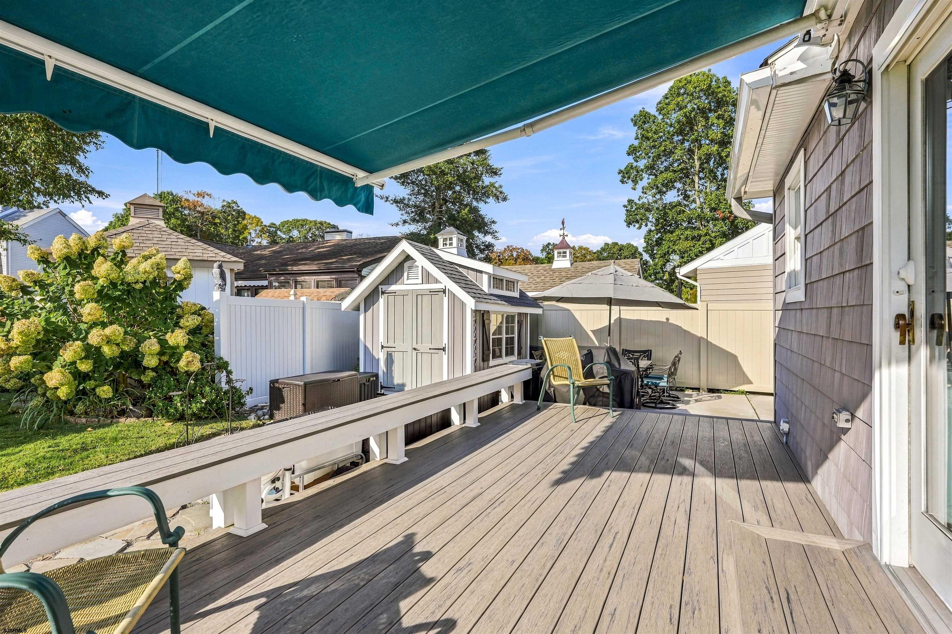 Wooden deck with a teal awning, outdoor seating, garden, and shed.