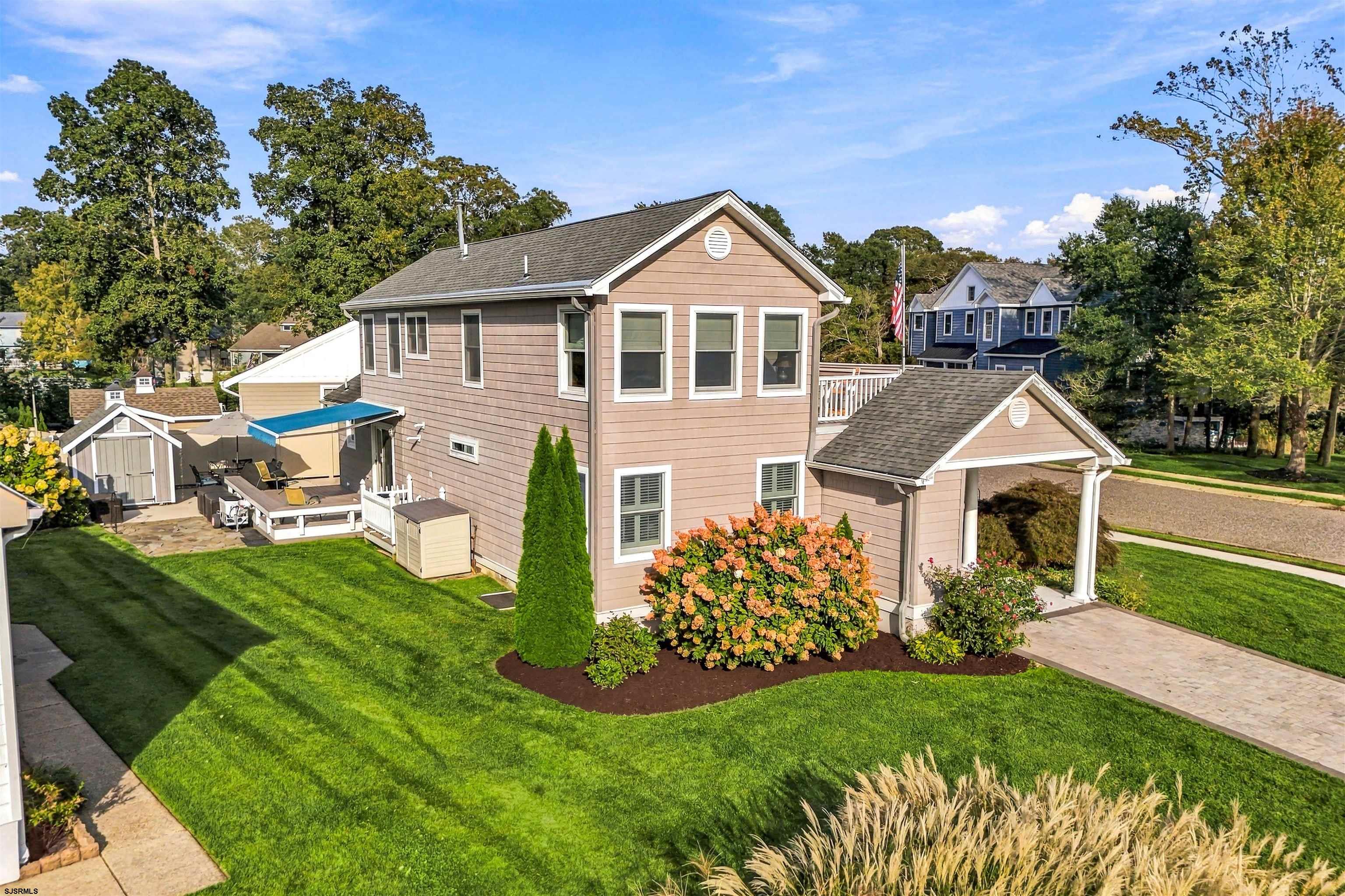 Two-story taupe house with a covered entry, landscaped lawn, and patio with a blue awning.