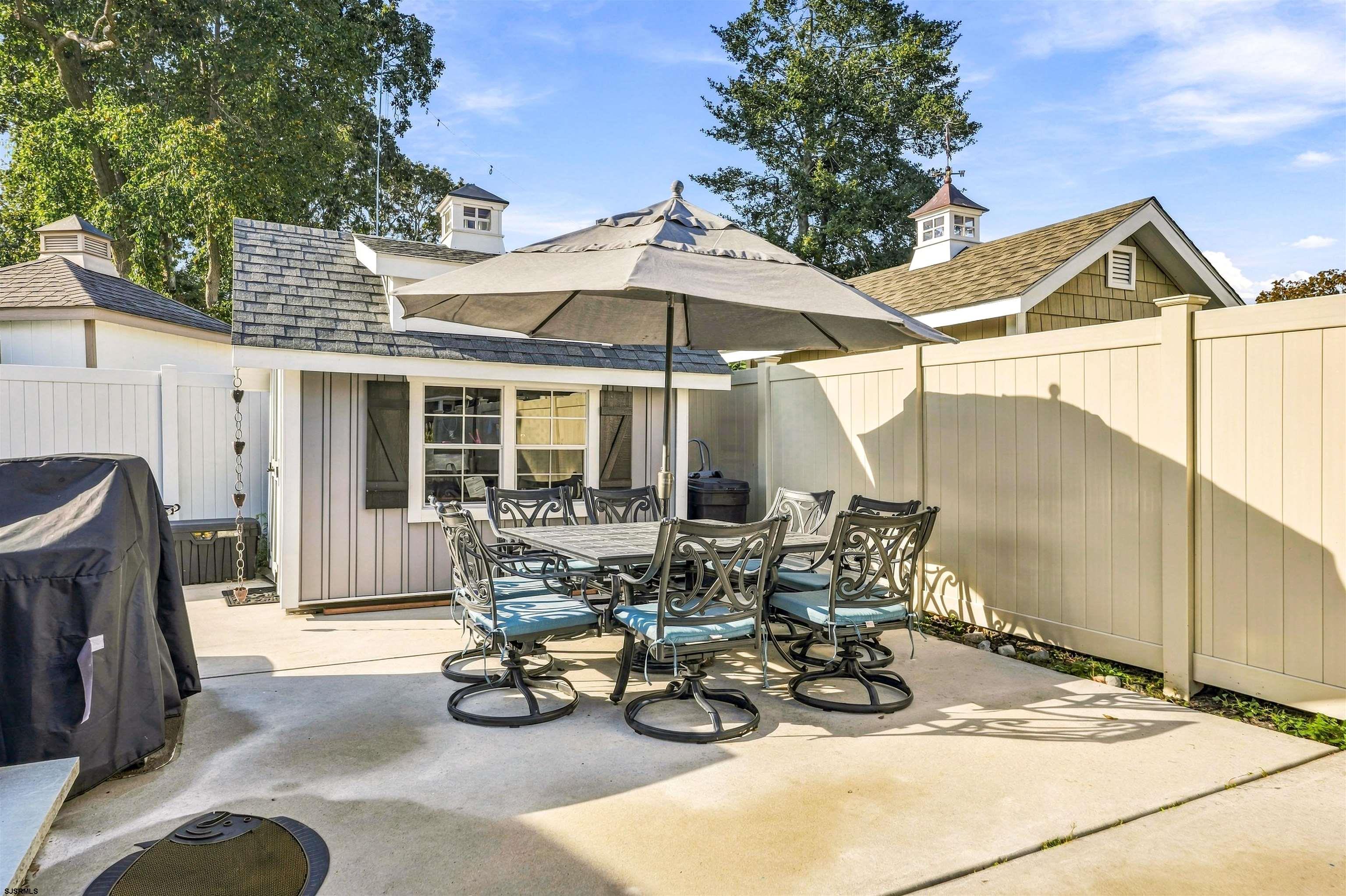 Fenced concrete patio with umbrella-shaded dining set and a small shed.