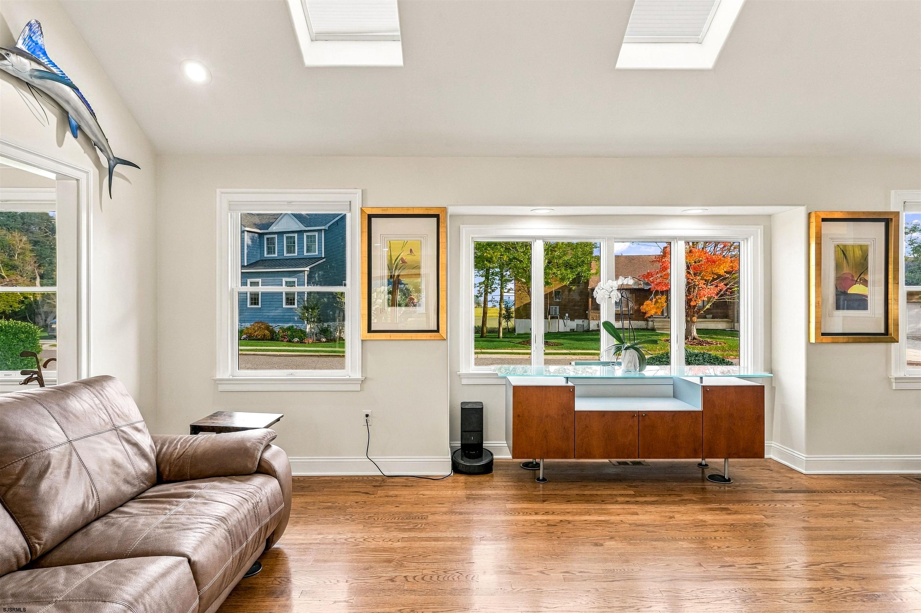 Living room with hardwood floors, skylights, leather sectional, and wide windows overlooking autumn trees.