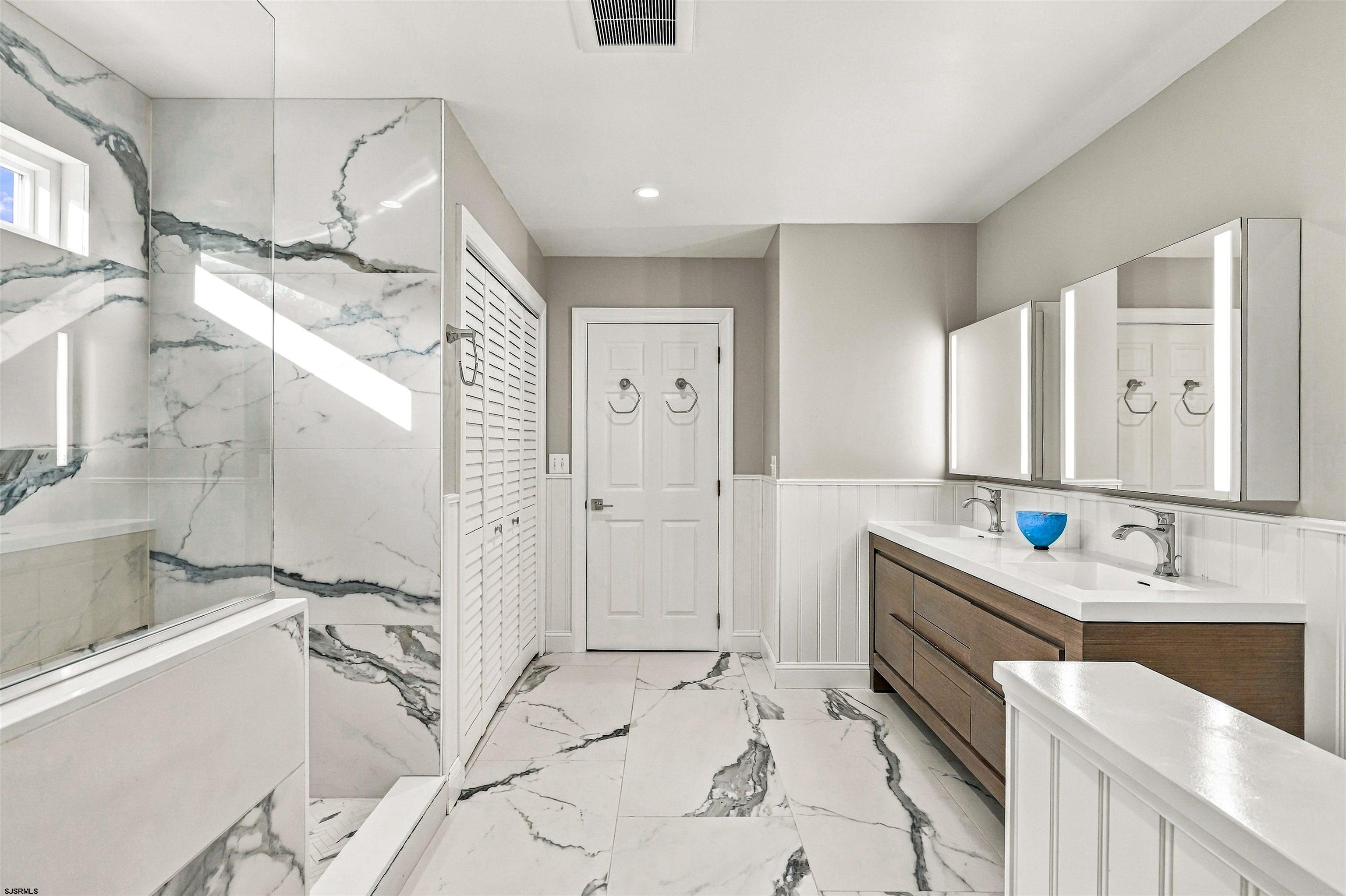 Bathroom with dramatic veined marble tile, glass shower, and double-sink wood vanity.