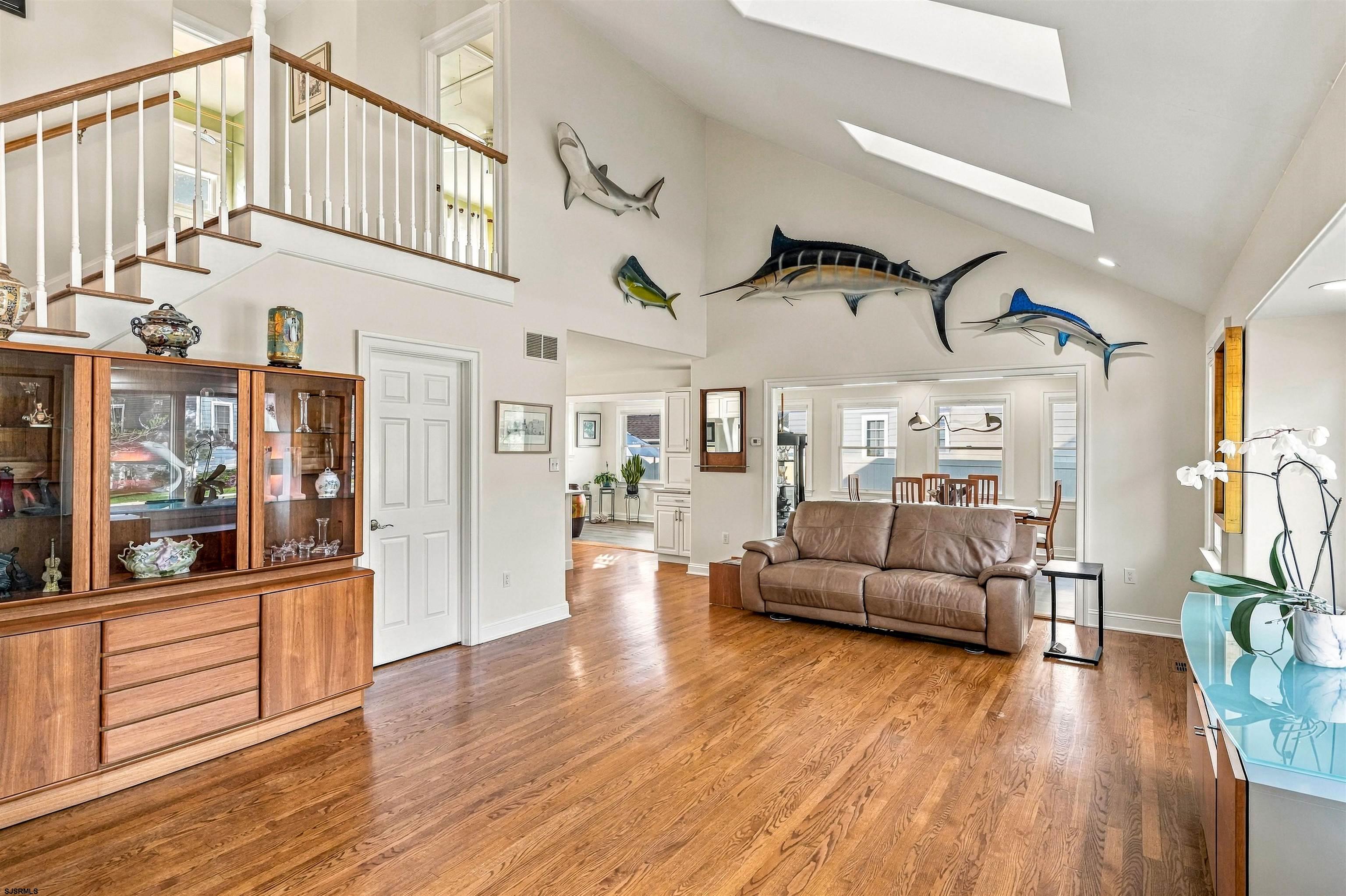 Vaulted living room with skylights, hardwood floors, mounted fish, and a brown leather sofa.