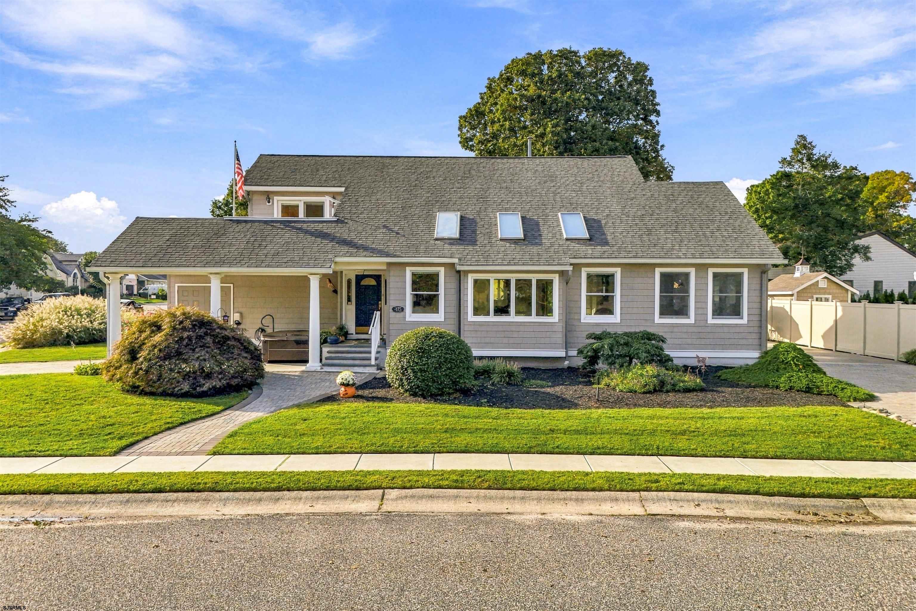 Gray-shingled house with a covered entry, skylights, landscaped lawn, and American flag.