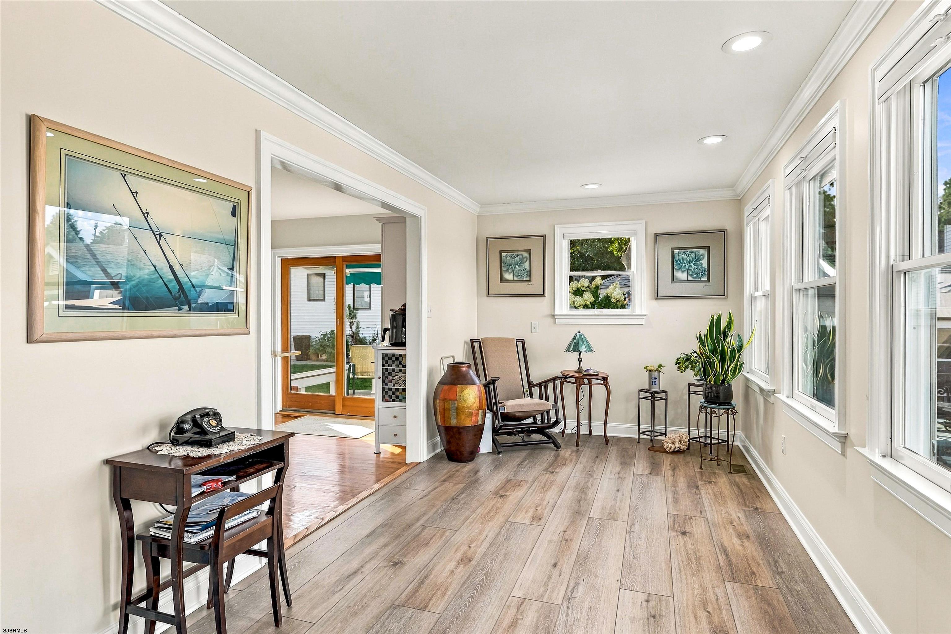 Sunlit sitting room with tall windows, wood-look floors, plants, and a sliding glass patio door.