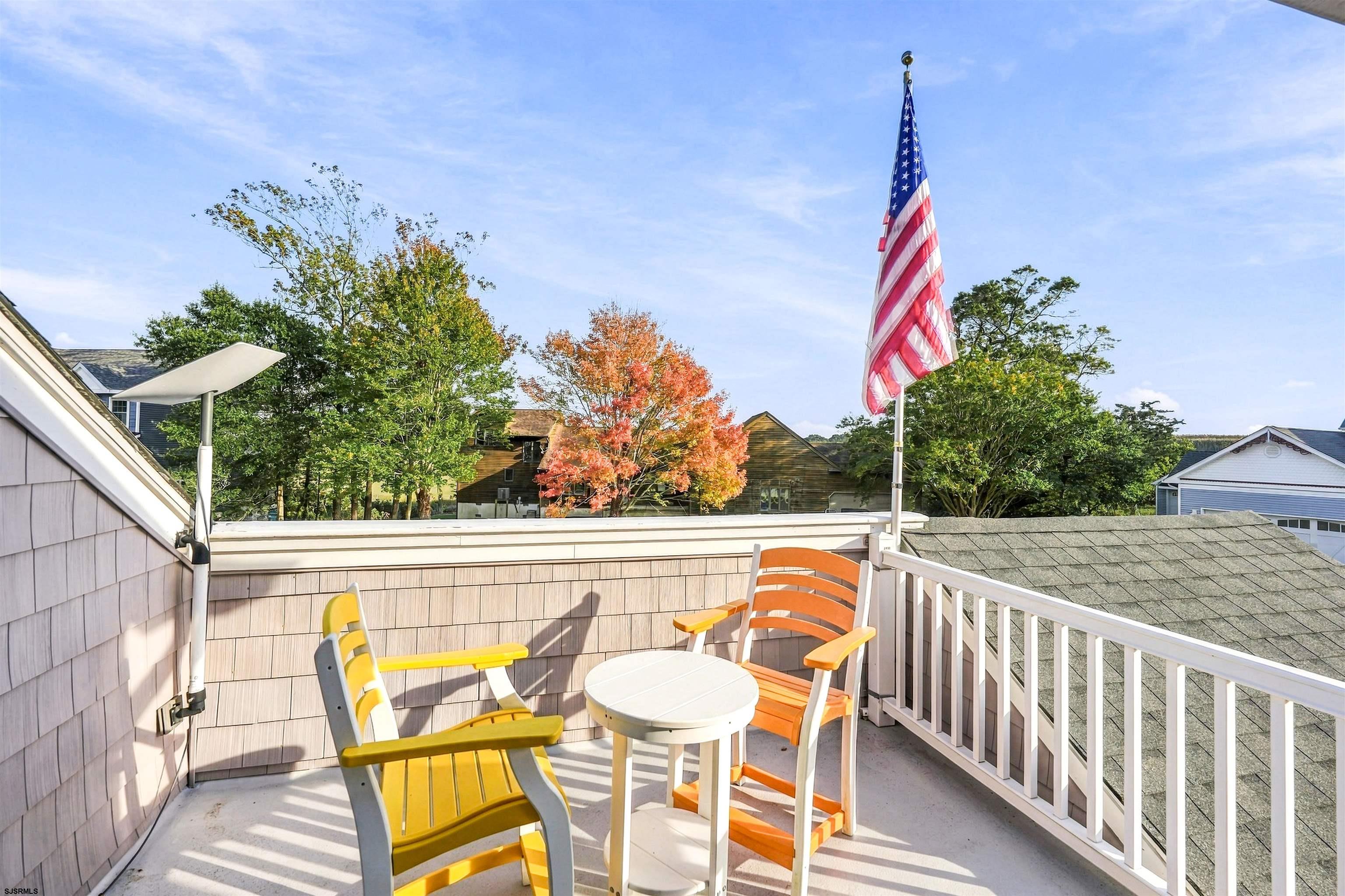 Rooftop deck with colorful chairs and an American flag overlooking autumn trees.