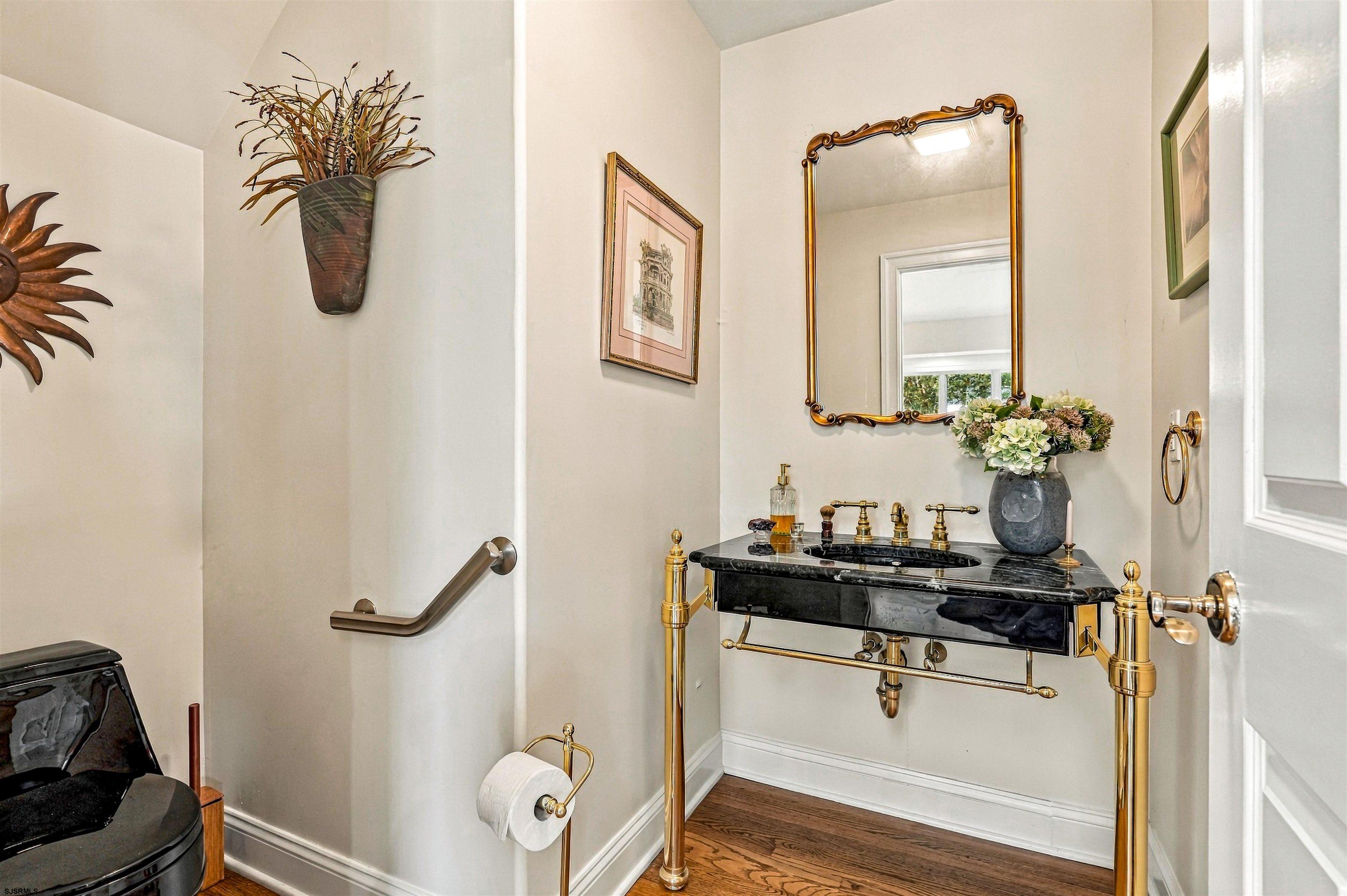 Powder room with a black marble console sink, ornate brass fixtures, and a gold-framed mirror.
