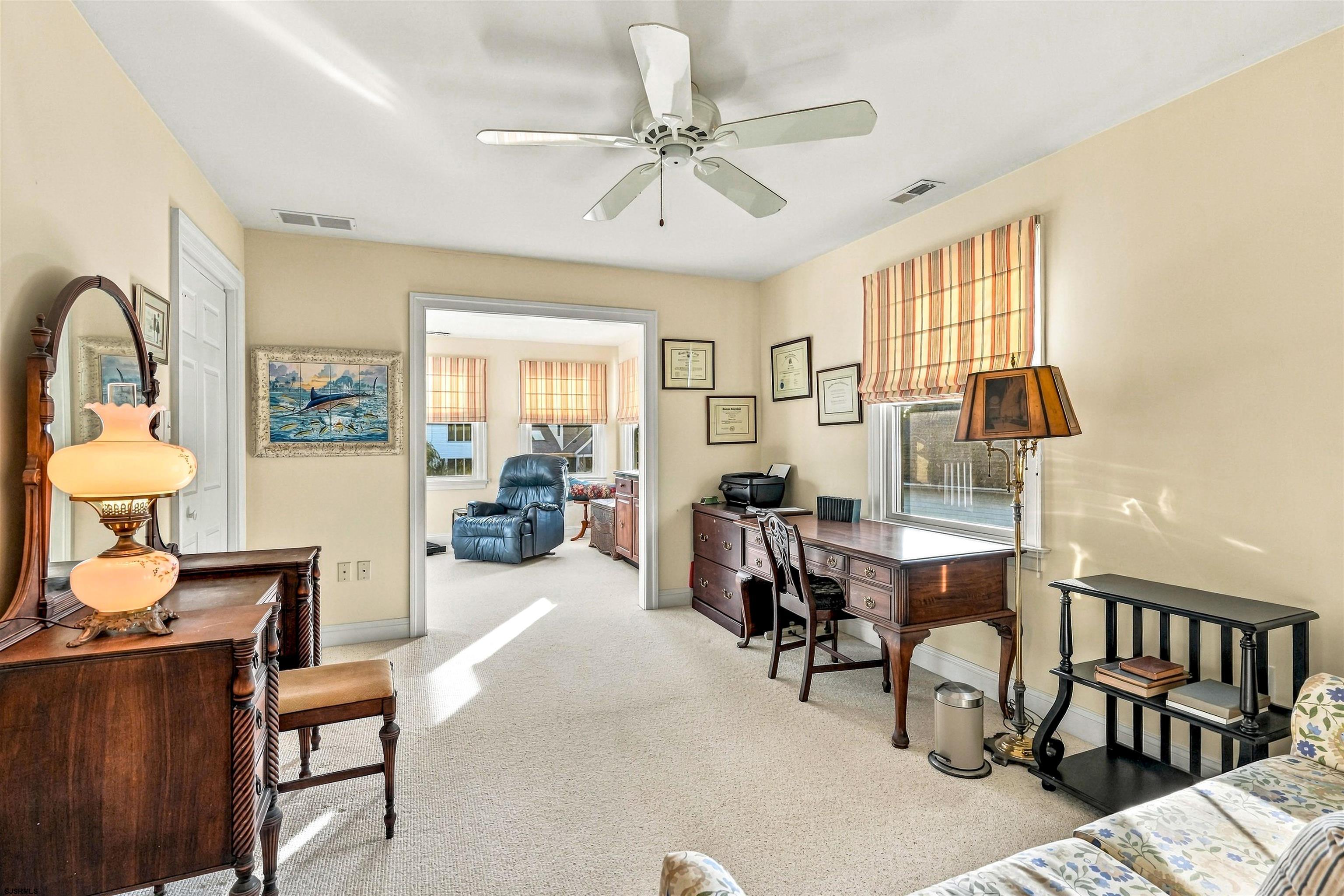 Furnished home office with a dark wood desk, antique dresser, and doorway to a sitting area.